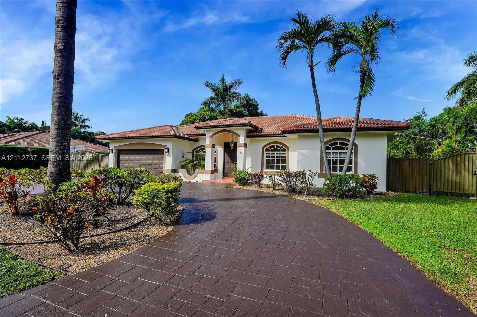 Single-story exterior featuring a clay tile roof, arched windows, an attached multi-car garage, and a stamped concrete driveway