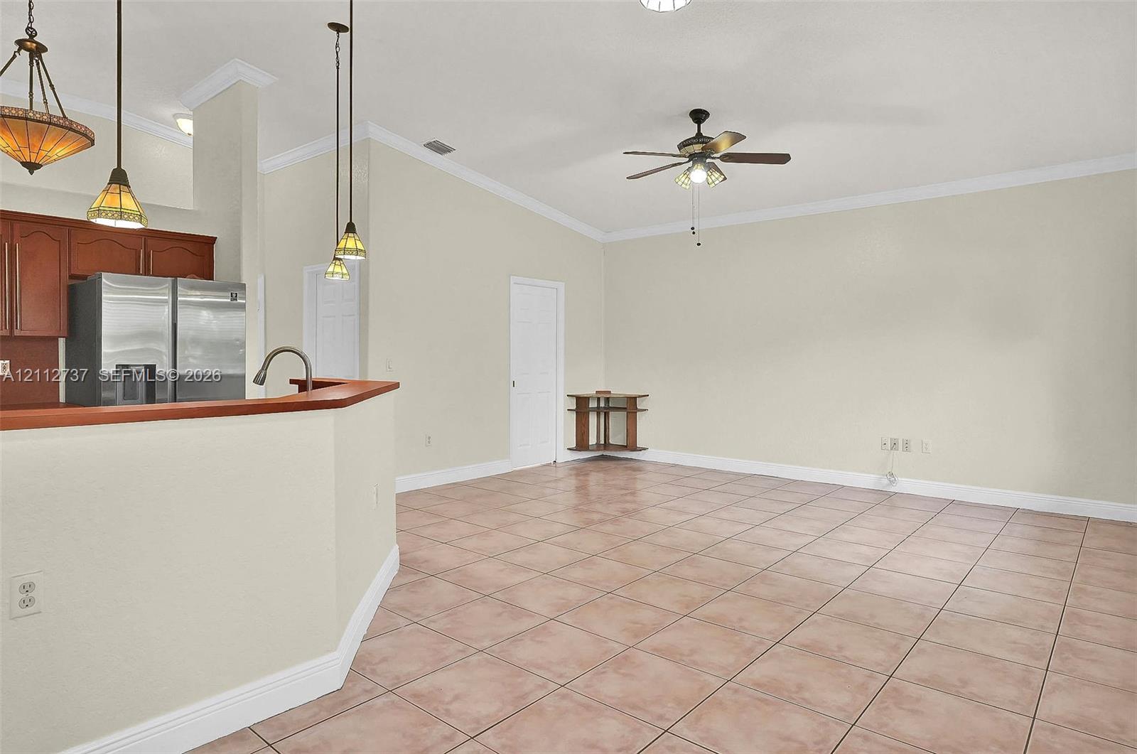 Open-concept space featuring tile flooring, vaulted ceilings with crown molding, a kitchen pass-through counter, pendant lighting, and a ceiling fan