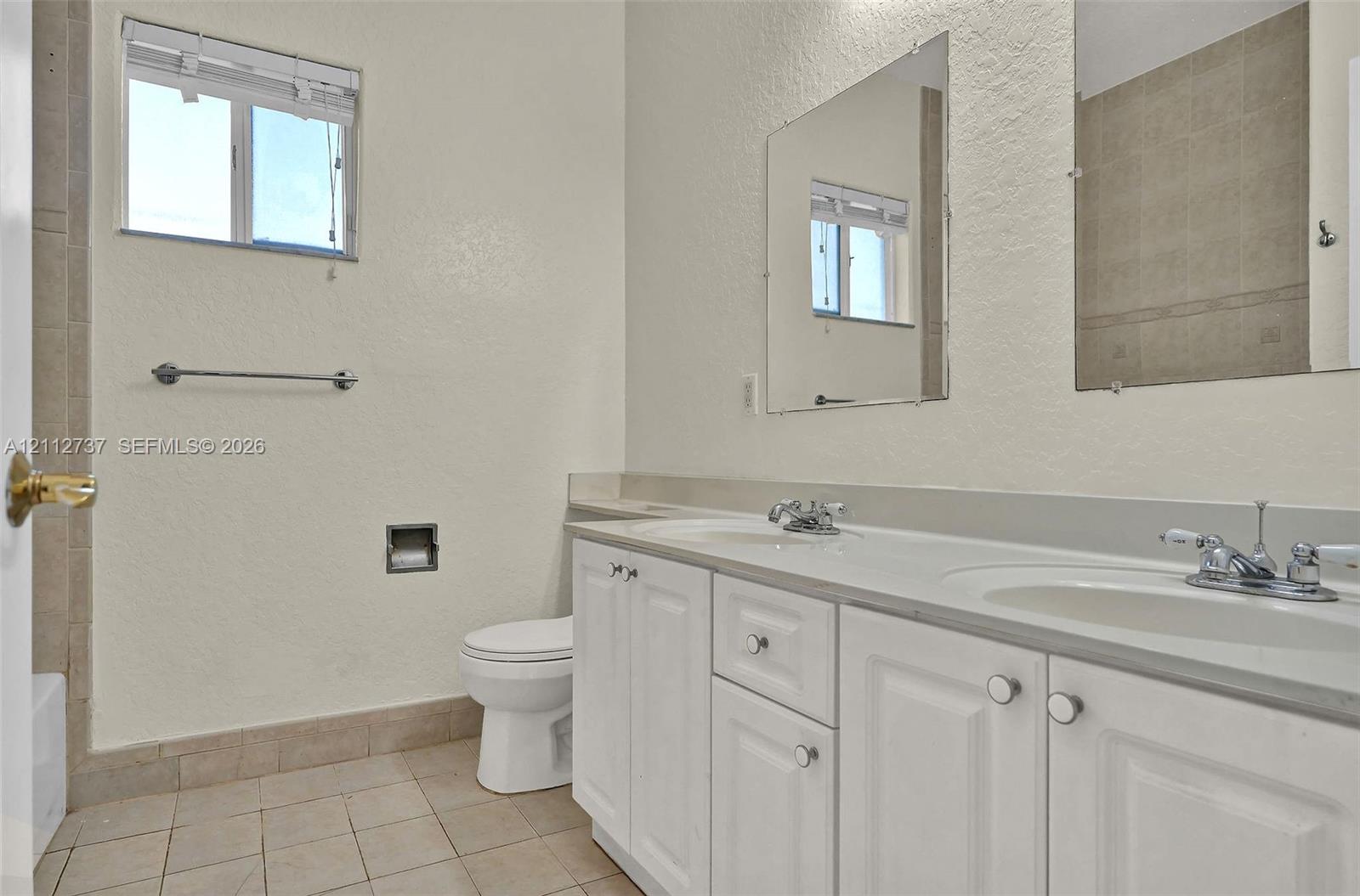 Dual-sink vanity with white cabinetry, light-toned countertop, and rectangular wall-mounted mirrors, complemented by tile flooring