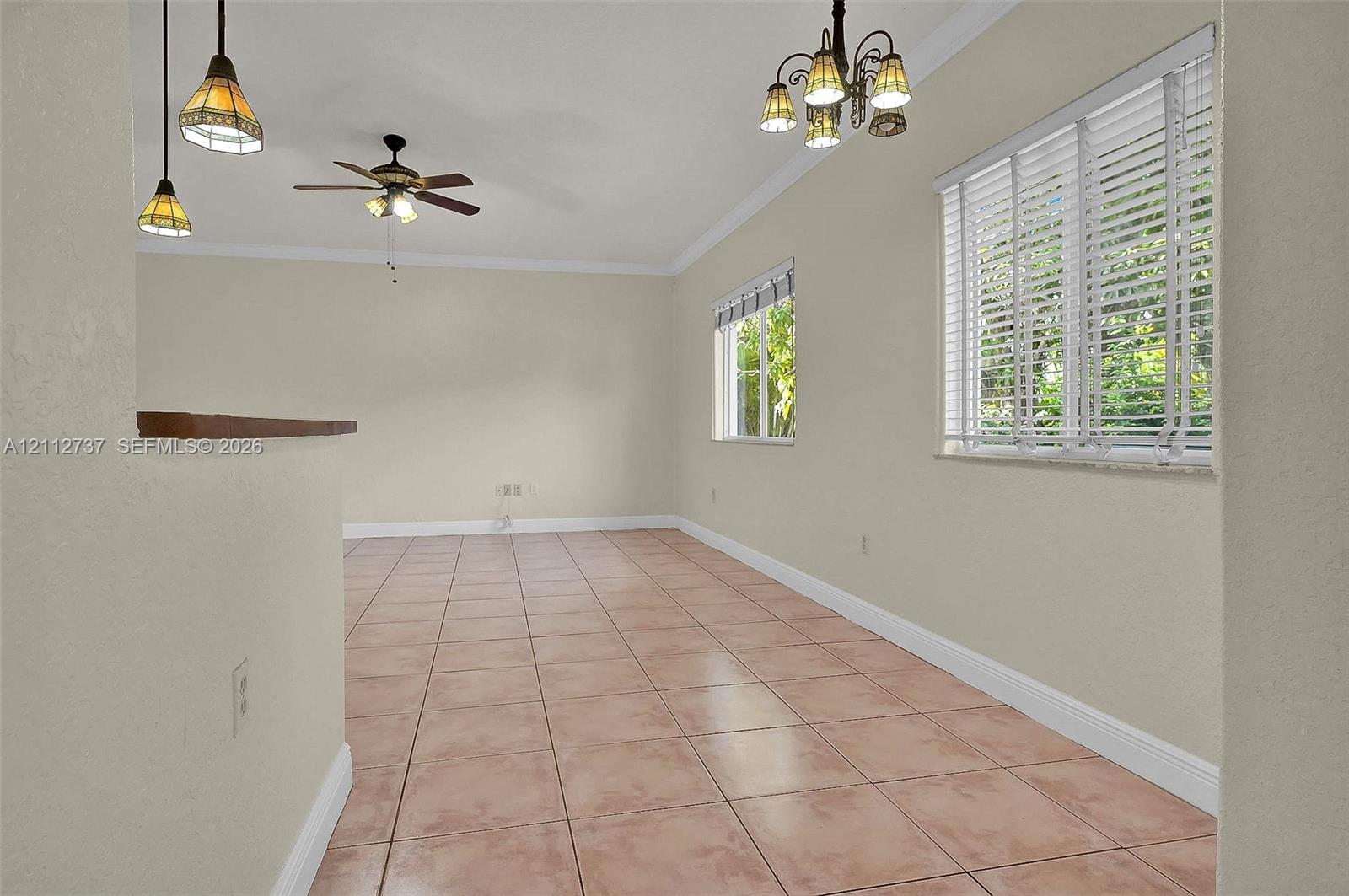 Interior space featuring tile flooring, crown molding, a multi-light chandelier, a ceiling fan with integrated lighting, and dual pendant lights over a pass-through opening