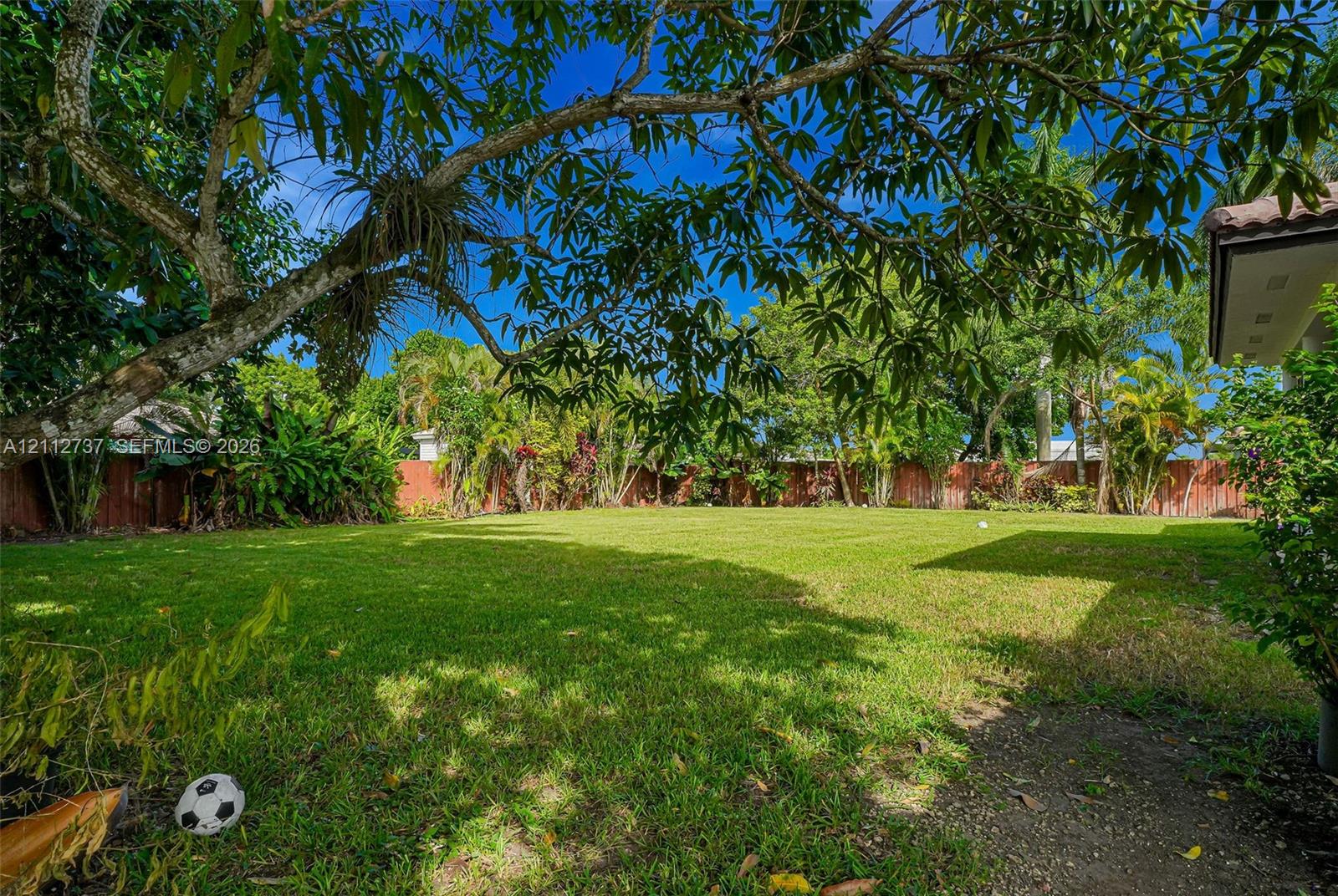 Expansive backyard featuring a manicured lawn, mature trees, and perimeter wood fencing