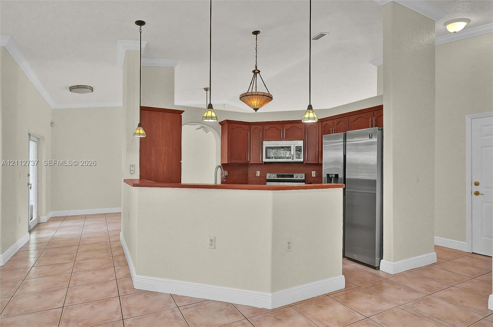 Kitchen featuring wood cabinetry, stainless steel appliances, tile flooring, crown molding, and pendant lighting