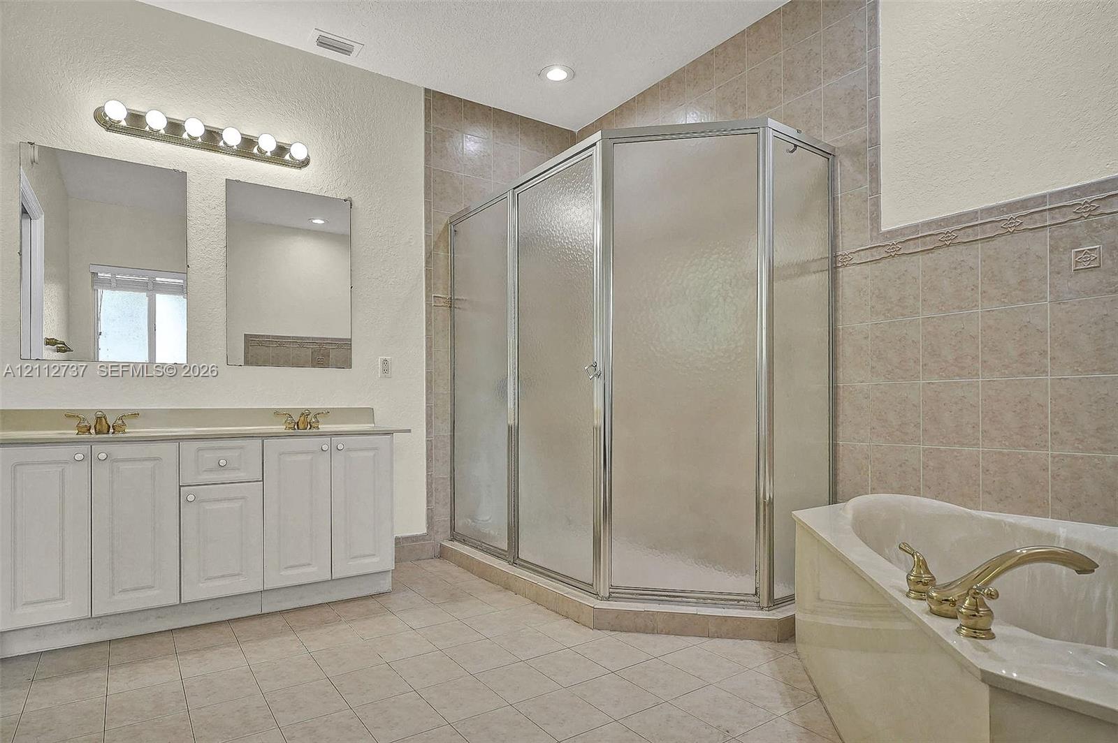Dual vanity with white cabinetry, corner shower enclosure with glass panels, separate soaking tub, and tile flooring