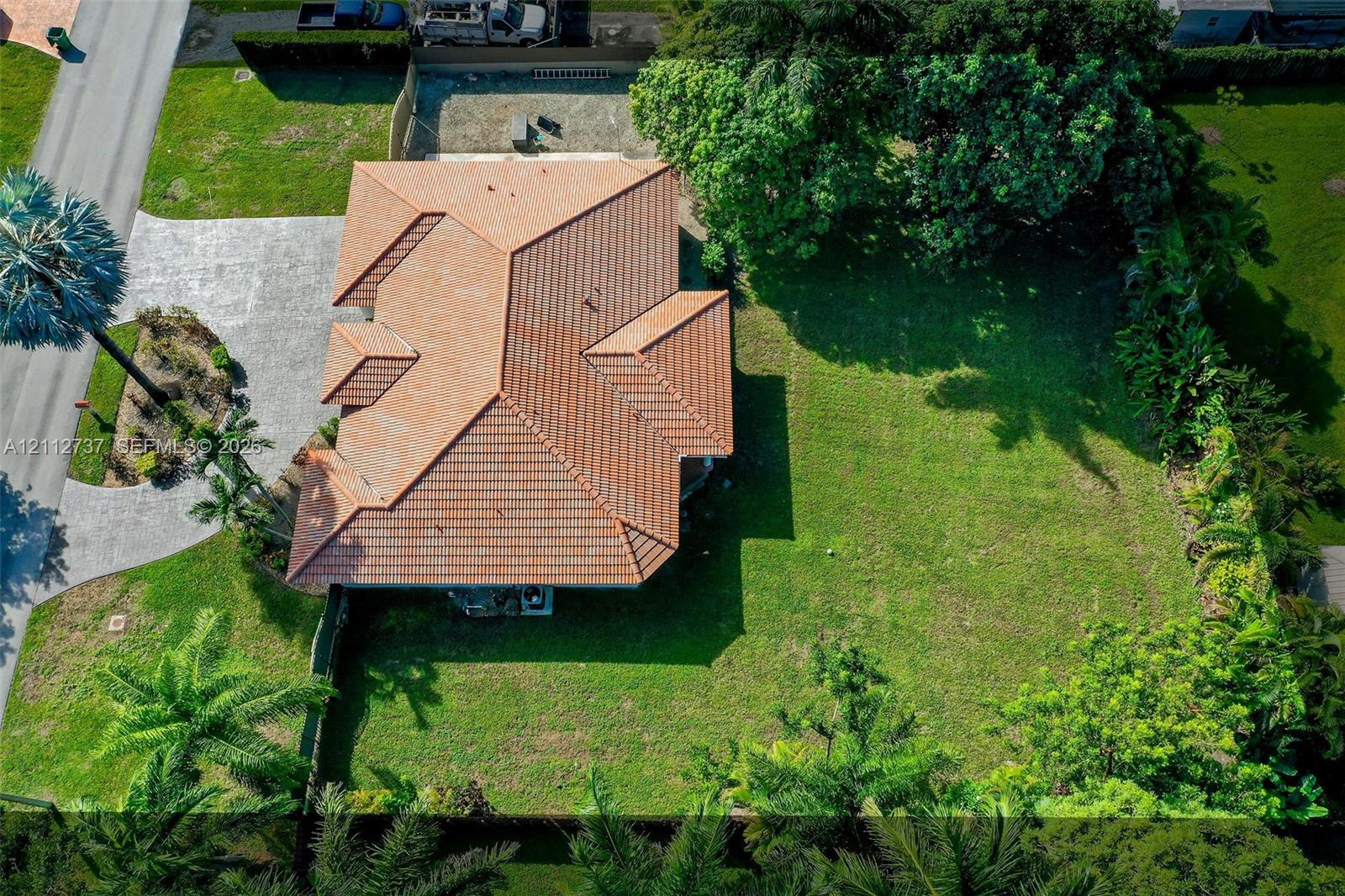 Aerial perspective featuring a tile roof, expansive grass lawn, paved driveway, and mature landscaping