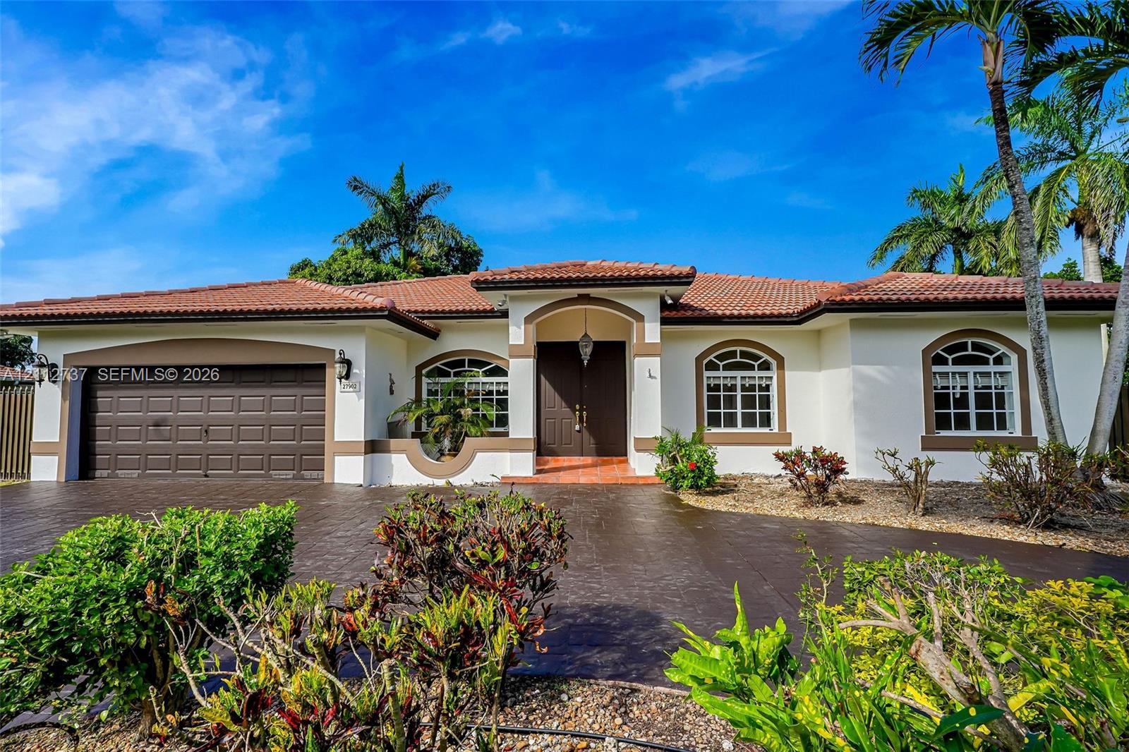 Stucco exterior featuring a tiled hip roof, arched window casings, double-door entryway, and a textured paver driveway Stucco exterior featuring a tiled hip roof, arched window casings, double-door entryway, and a textured paver driveway