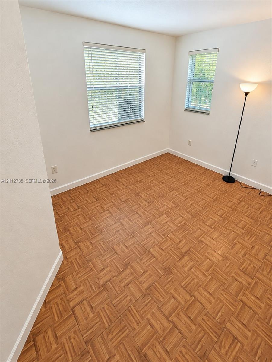 Parquet wood-finish flooring, neutral walls, and two windows featuring horizontal blinds