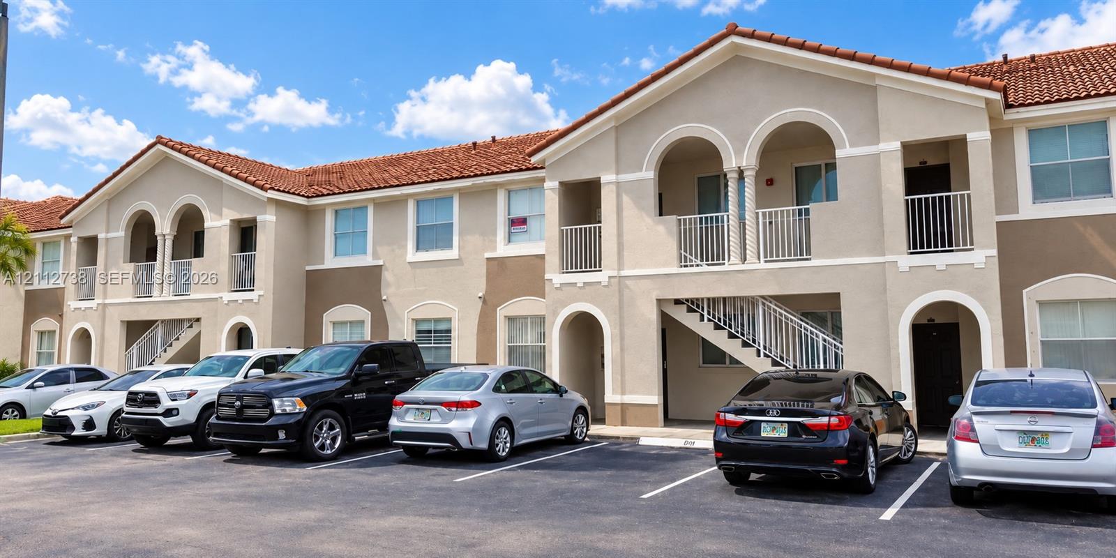 Stucco exterior featuring mission-style red tile roofing, arched architectural accents, and private balconies with metal railings Stucco exterior featuring mission-style red tile roofing, arched architectural accents, and private balconies with metal railings