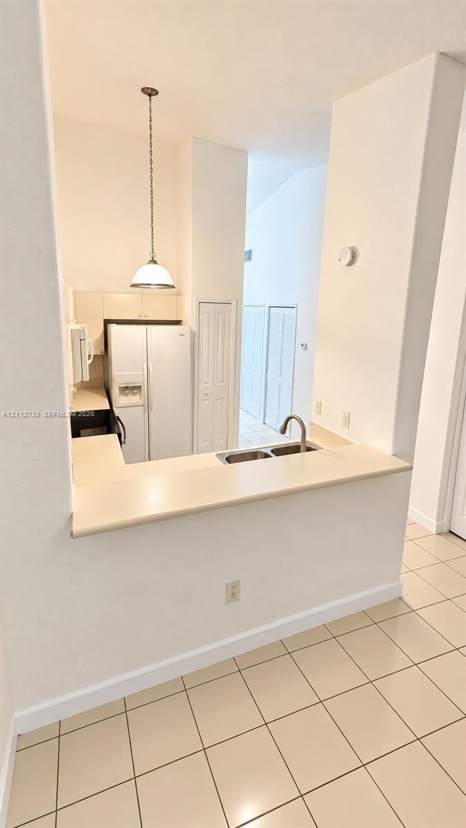 Kitchen featuring a pass-through counter, double-basin stainless steel sink, tile flooring, built-in cabinetry, and a pendant light fixture Kitchen featuring a pass-through counter, double-basin stainless steel sink, tile flooring, built-in cabinetry, and a pendant light fixture
