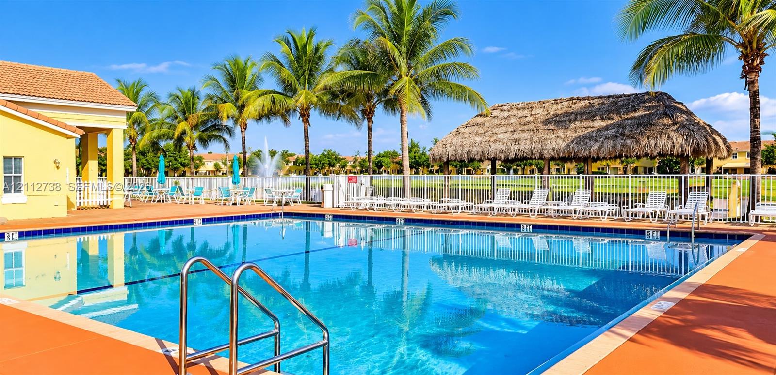 In-ground swimming pool with metal ladder entry, terracotta-toned deck, thatched-roof cabana, water fountain, and perimeter fencing In-ground swimming pool with metal ladder entry, terracotta-toned deck, thatched-roof cabana, water fountain, and perimeter fencing