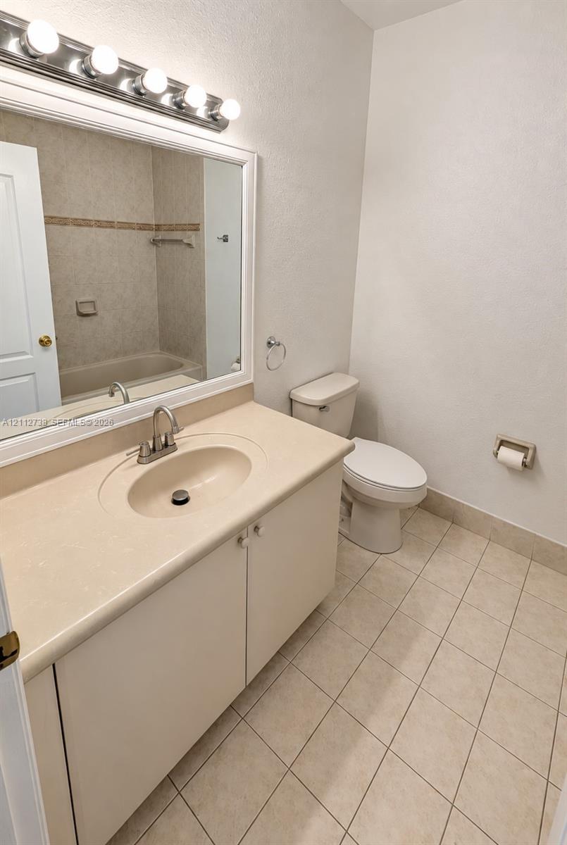 Bathroom featuring a vanity with integrated sink and countertop, large framed wall mirror, multi-bulb overhead lighting, and ceramic tile flooring