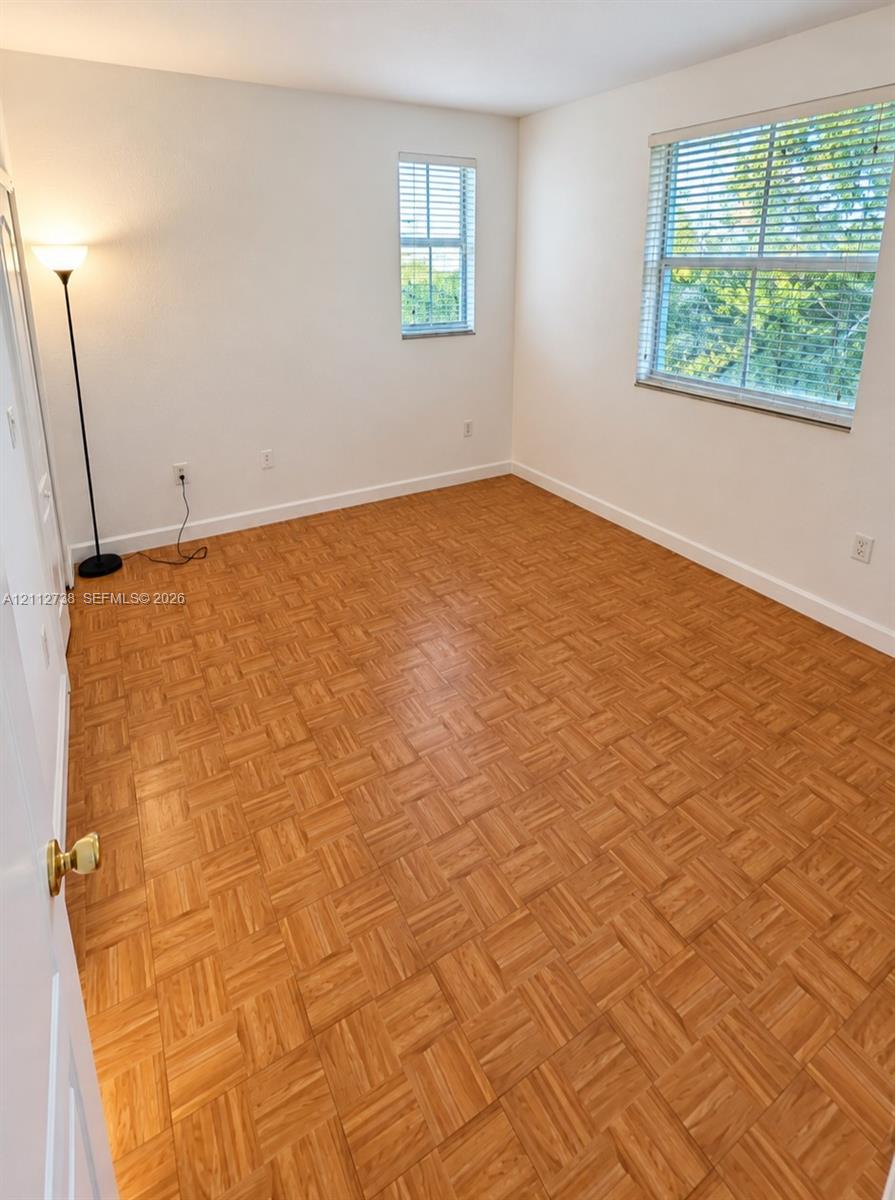 Parquet wood-finish flooring, neutral wall tones, and multiple windows with horizontal blinds