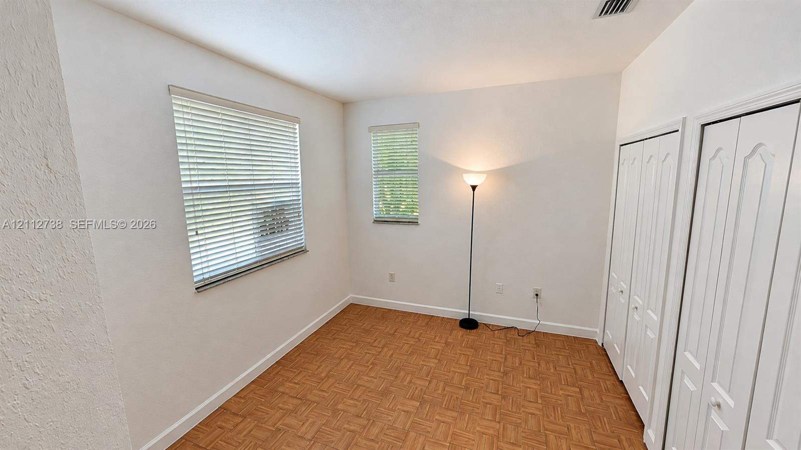 Room featuring parquet wood-finish flooring, two windows with horizontal blinds, and dual bi-fold closet doors
