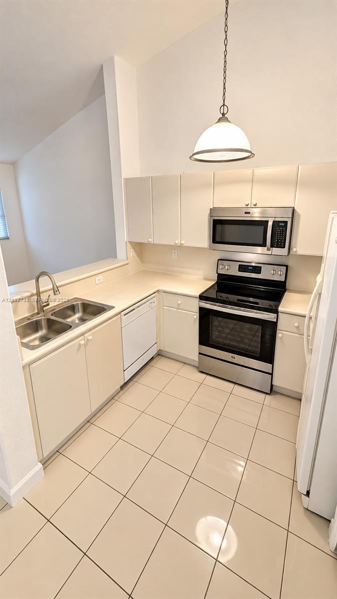 Kitchen featuring neutral-toned cabinetry, stainless steel appliances, ceramic tile flooring, a dual-basin stainless steel sink, and a dome pendant light fixture