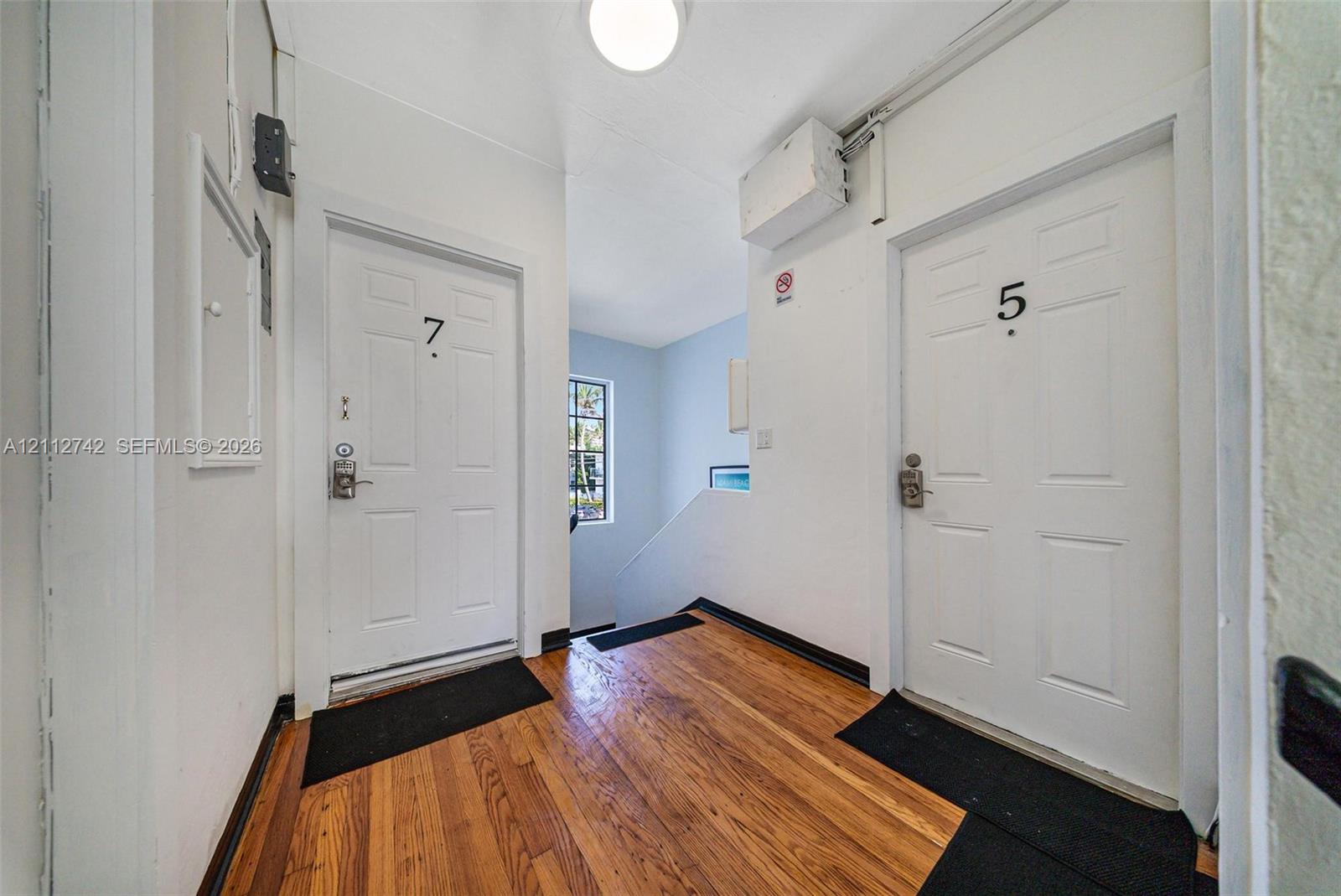 Common area featuring wood-finish flooring, two six-panel entry doors, flush-mount ceiling lighting, and a windowed staircase