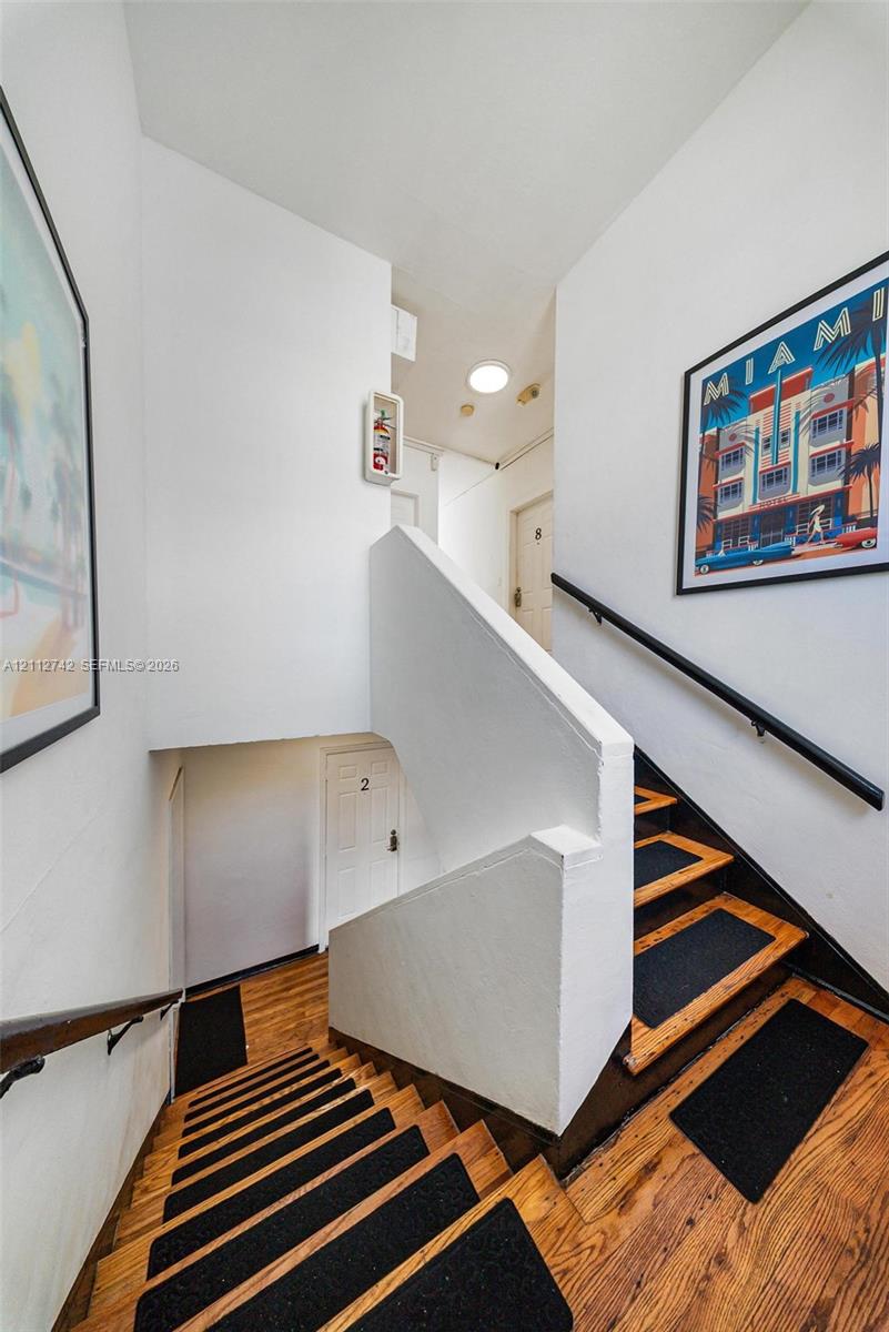 Stairwell featuring wood-finish treads, matte black handrails, and flush-mount ceiling lighting