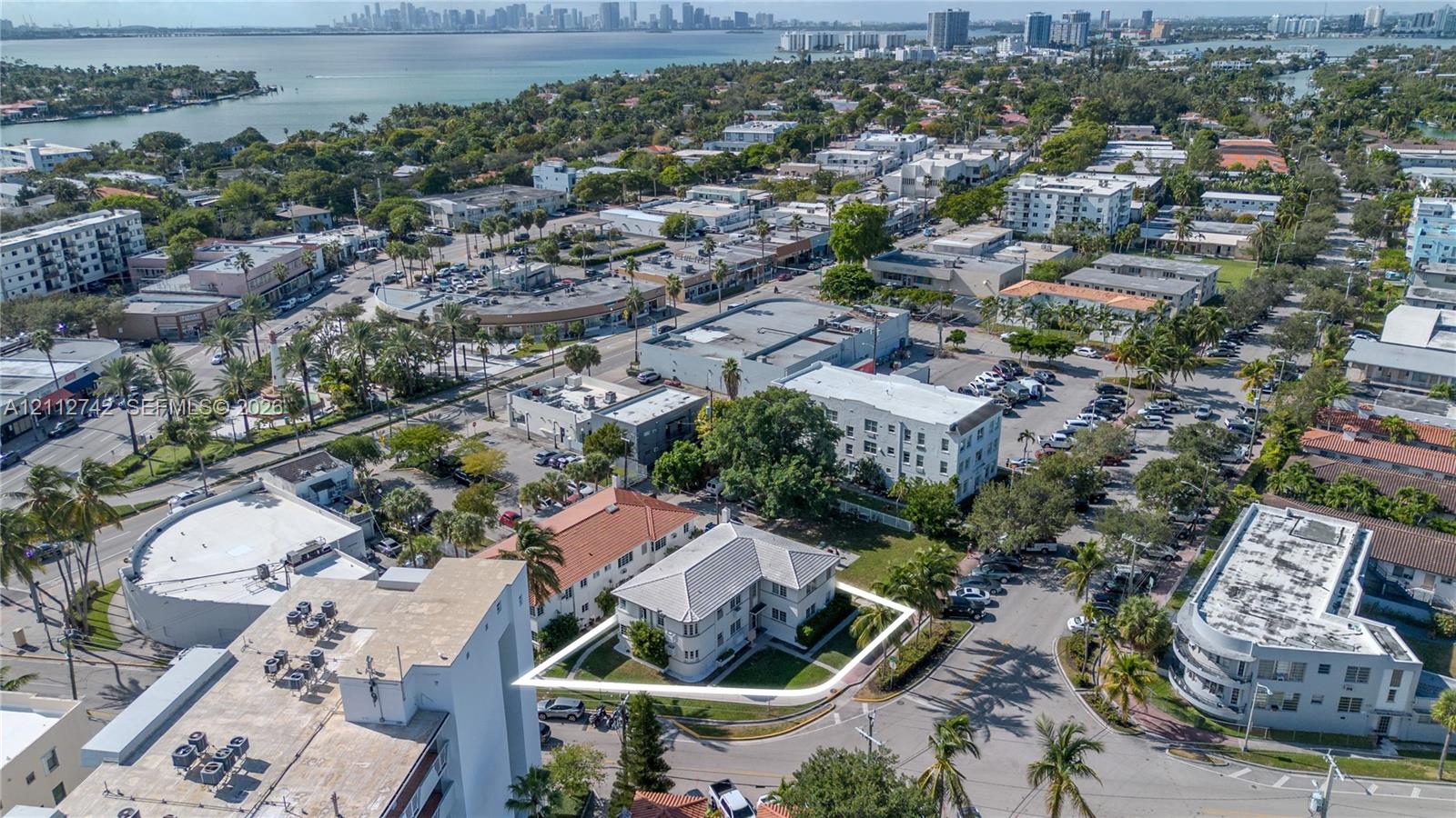 Aerial perspective of a multi-story property featuring a hip roof, exterior masonry construction, surrounding lawn space, and mature perimeter trees