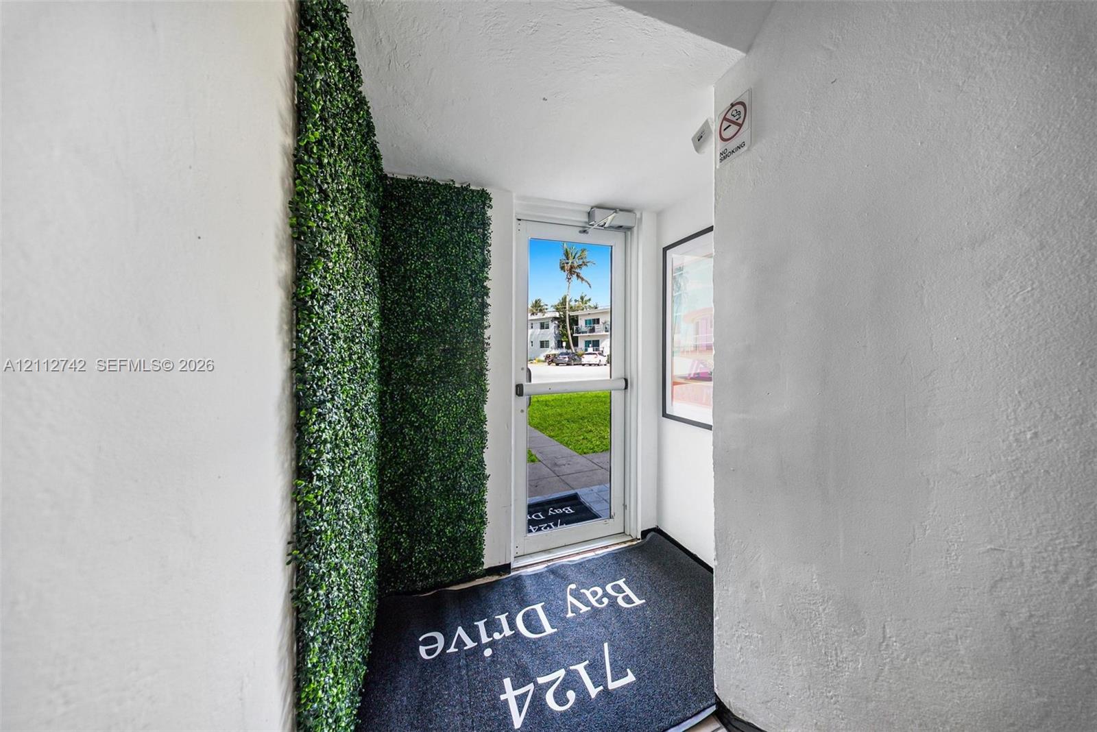 Entryway featuring an artificial green wall accent and a full-glass commercial-style door with a panic bar handle