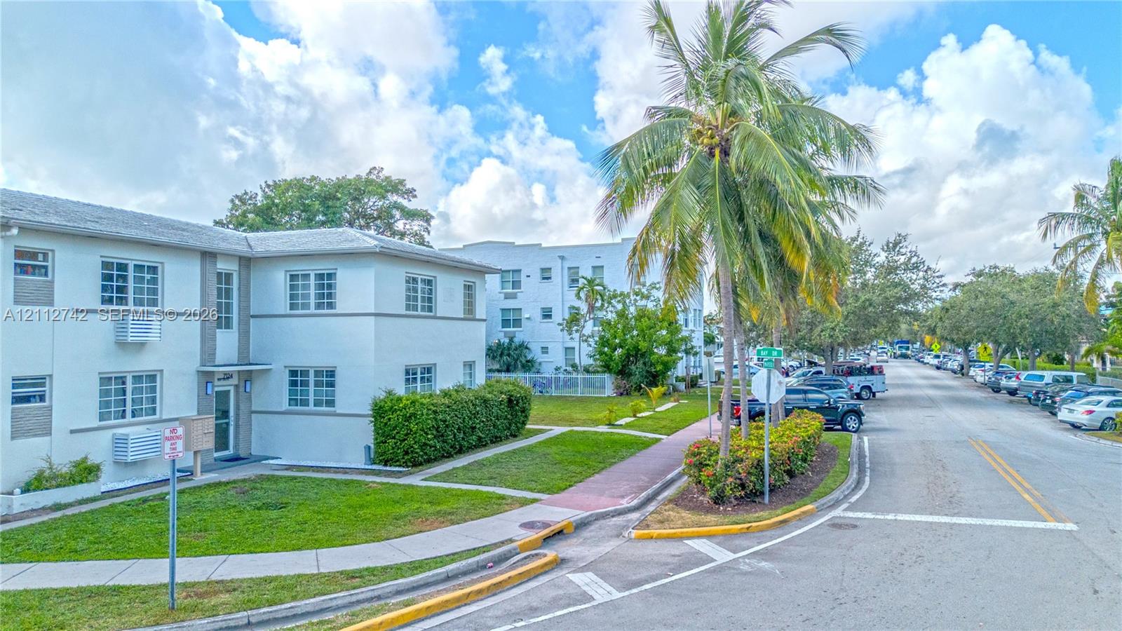 Two-story building exterior featuring smooth stucco finish, multi-pane windows, and landscaped grounds with mature palm trees