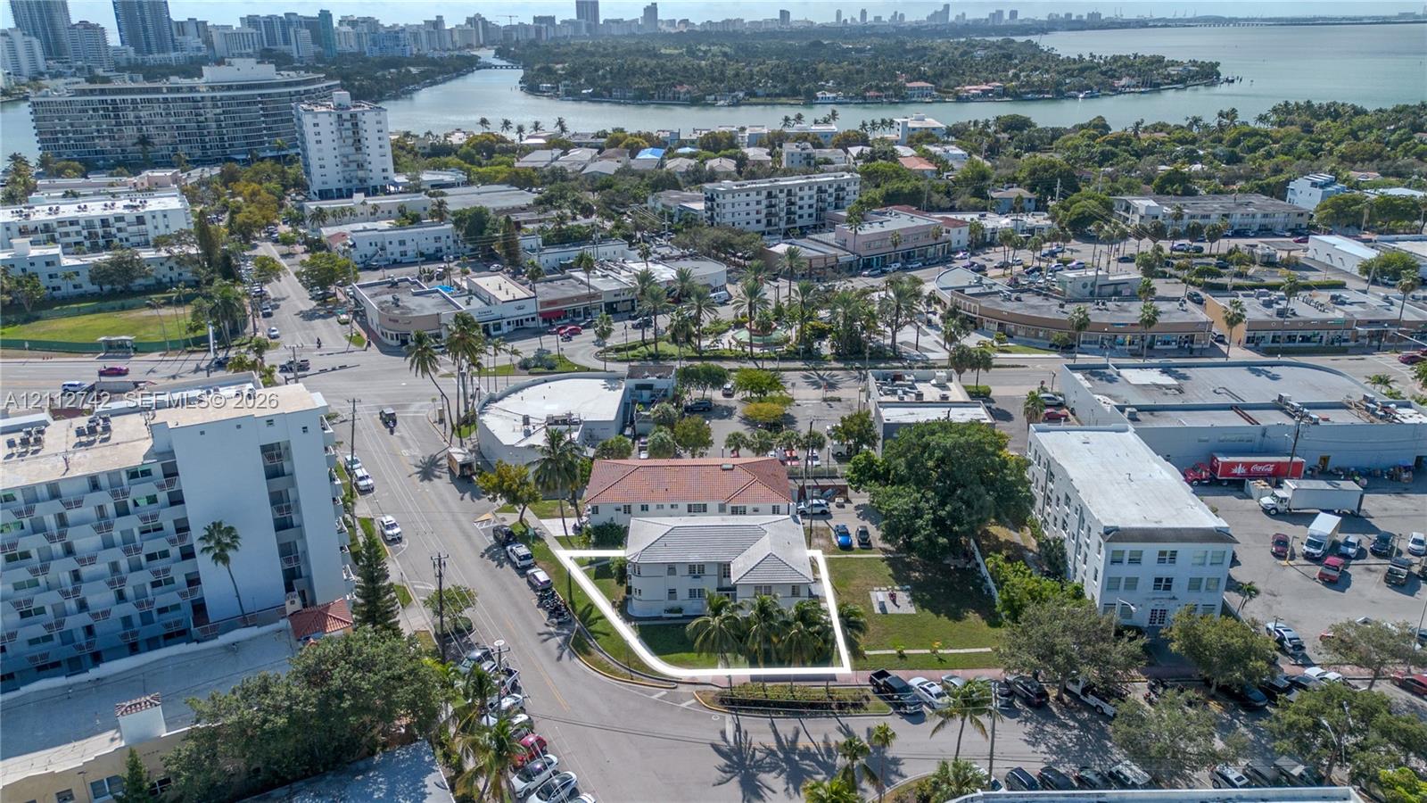 Aerial perspective featuring a multi-story building with a light-toned exterior, a hipped roof, on-site surface parking, and manicured green space