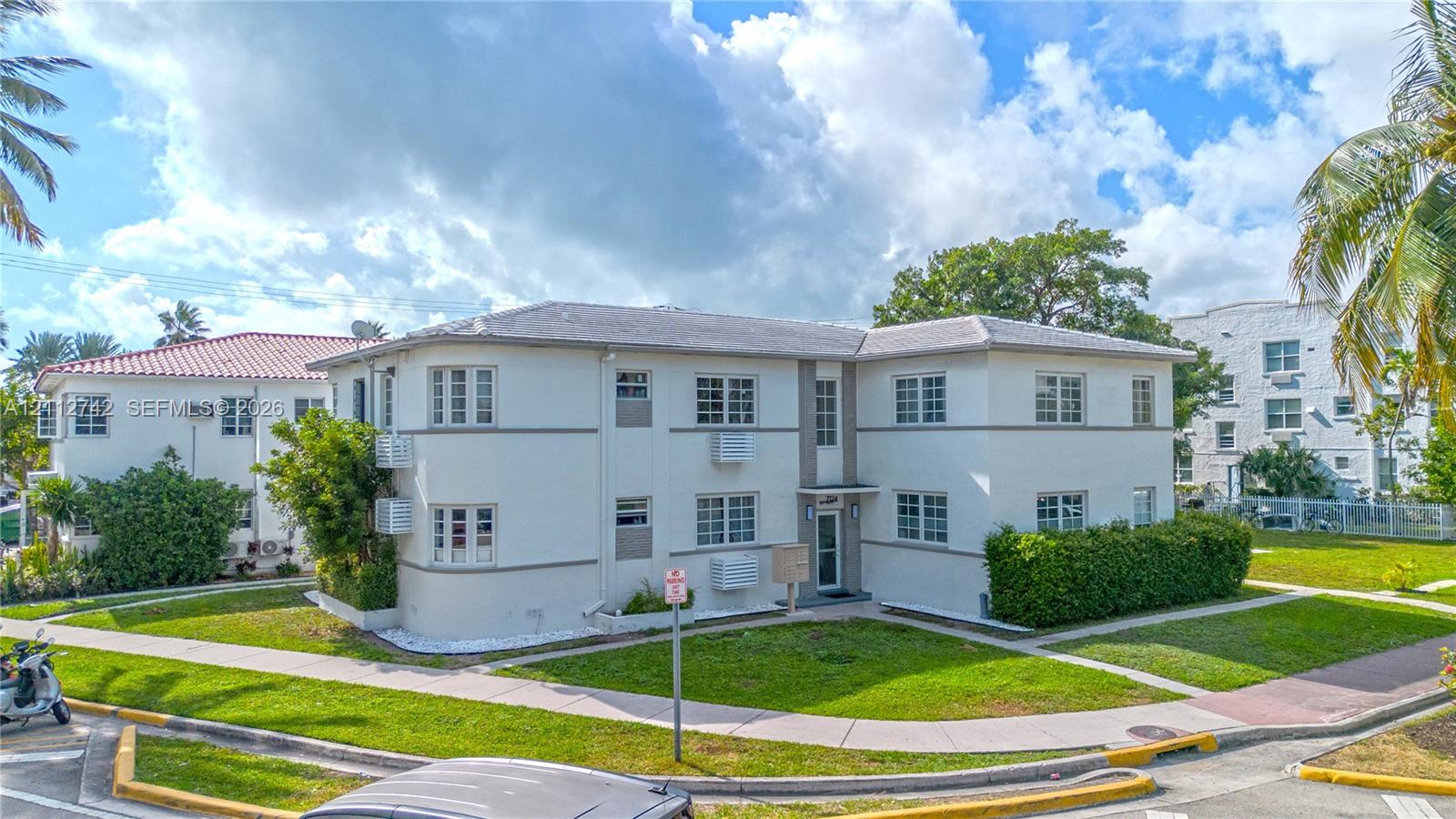 Two-story multi-family exterior featuring light-toned stucco walls, a rounded architectural corner, a neutral-toned hip roof, and grid-pane windows