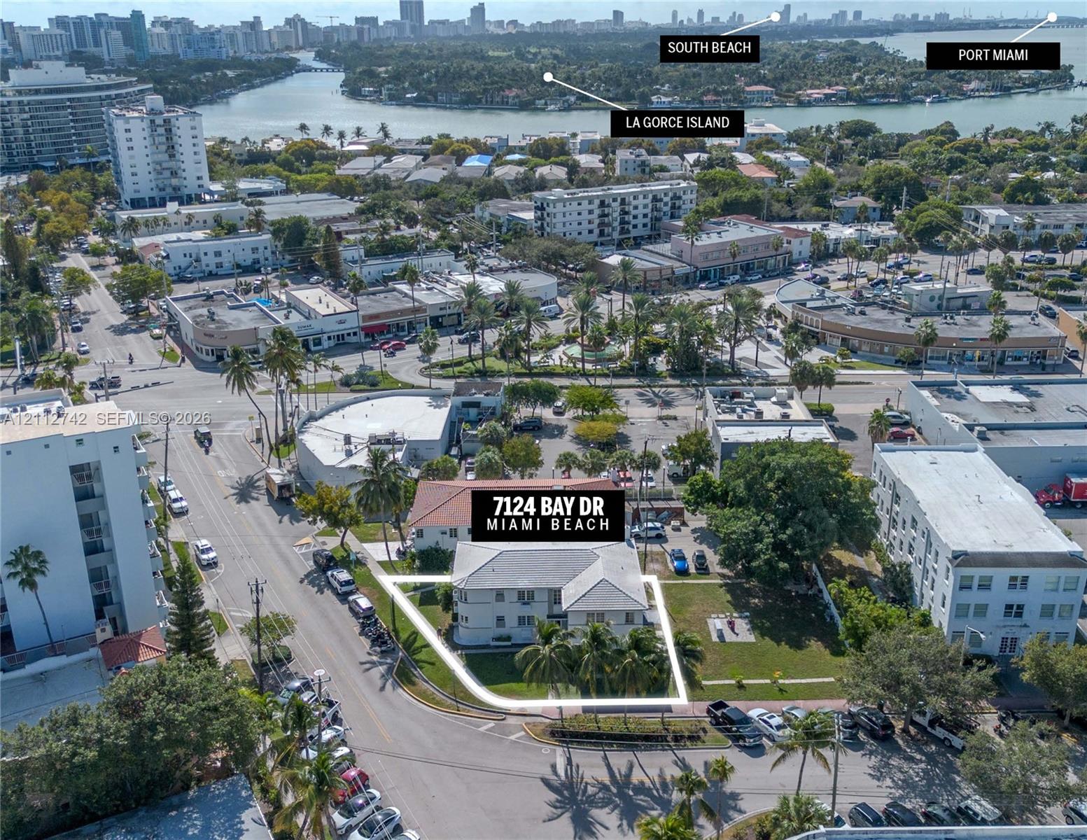 Aerial perspective of a multi-unit property featuring a corner lot location, light-toned exterior finish, gabled roofline, mature palm trees, and perimeter lawn area