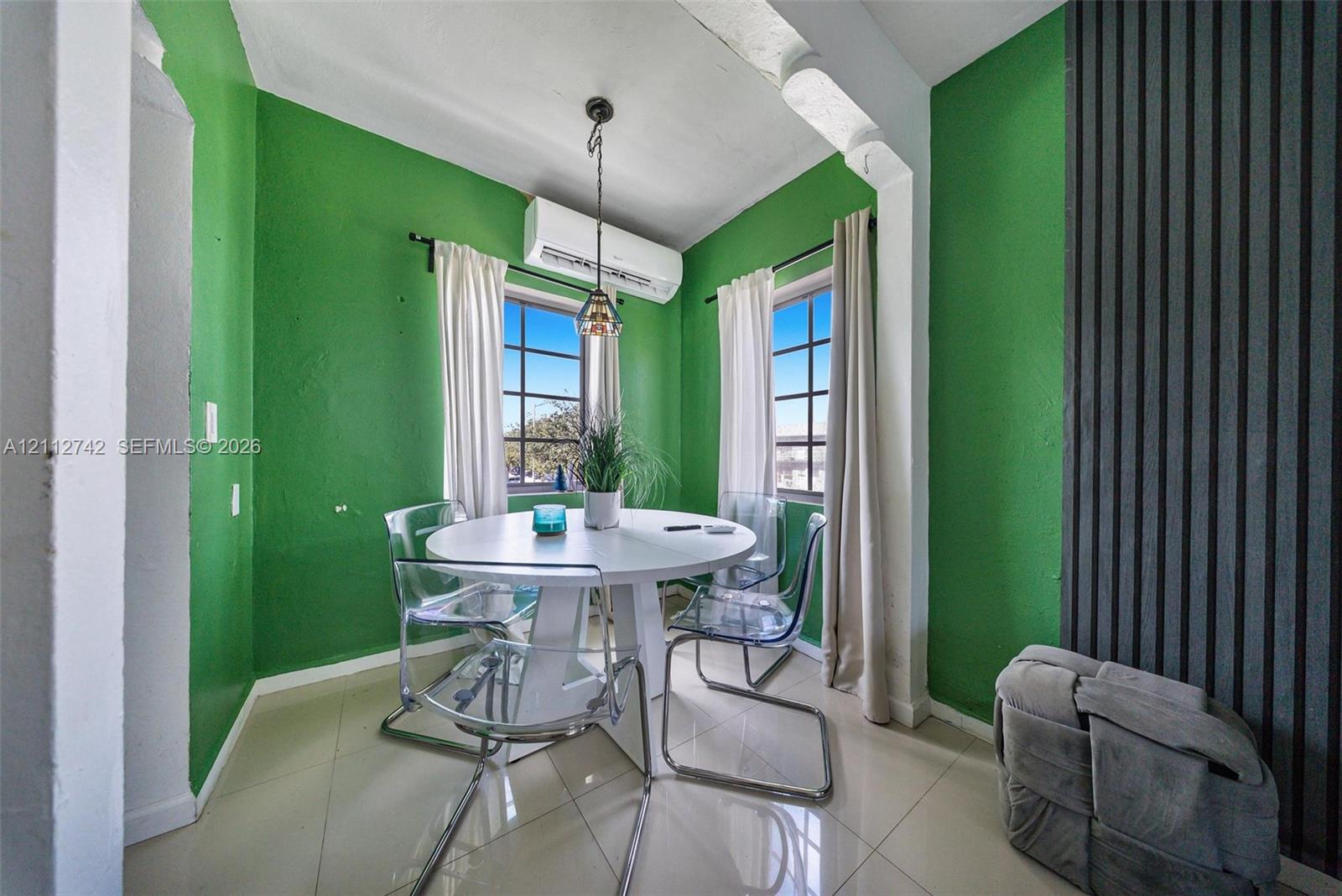 Neutral tile flooring, multi-pane windows, wall-mounted ductless climate control unit, hanging pendant light fixture, and vertical slat accent wall