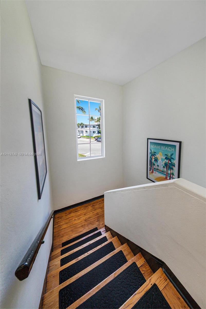 Staircase featuring wood-finish treads, contrasting textured inserts, a wall-mounted dark wood handrail, and a vertical window