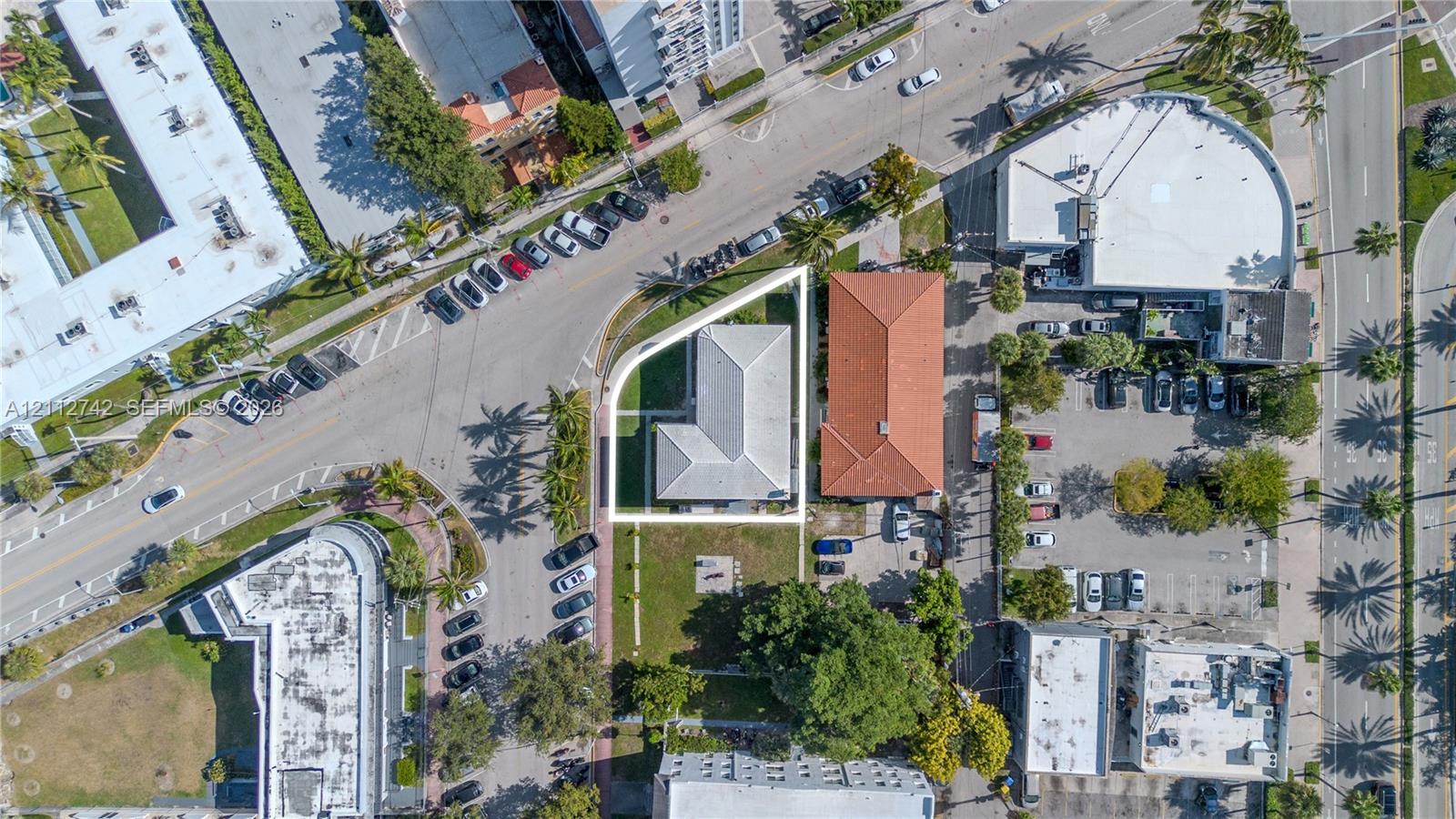 Corner lot featuring an L-shaped structure, a light-toned hipped roof, and mature perimeter landscaping