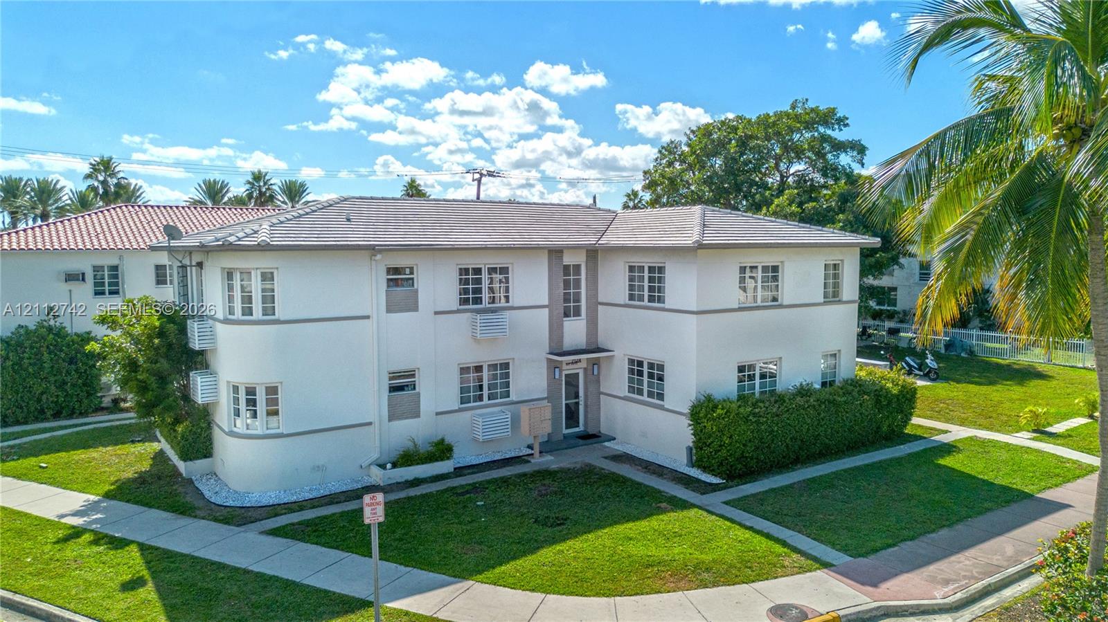 Two-story exterior featuring a smooth stucco facade, hip roof with charcoal-toned shingles, rounded corner architectural detail, multi-pane windows, and concrete walkways