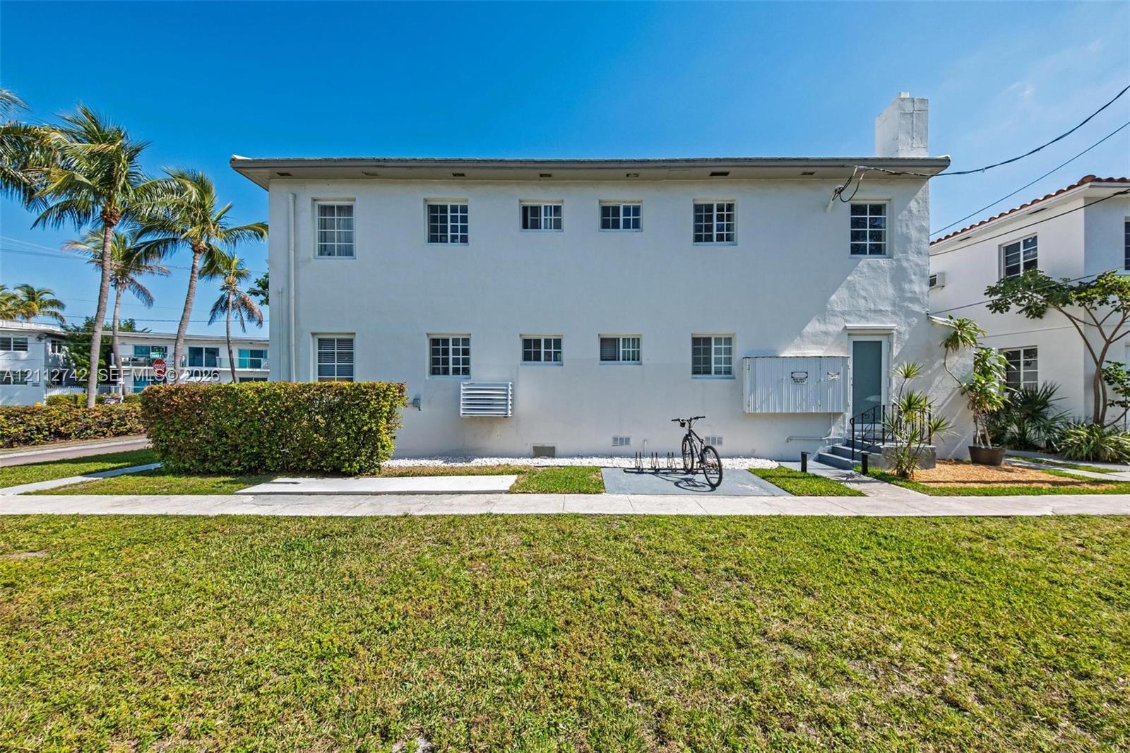 Two-story exterior featuring white stucco finish, multi-pane windows, and manicured hedge landscaping