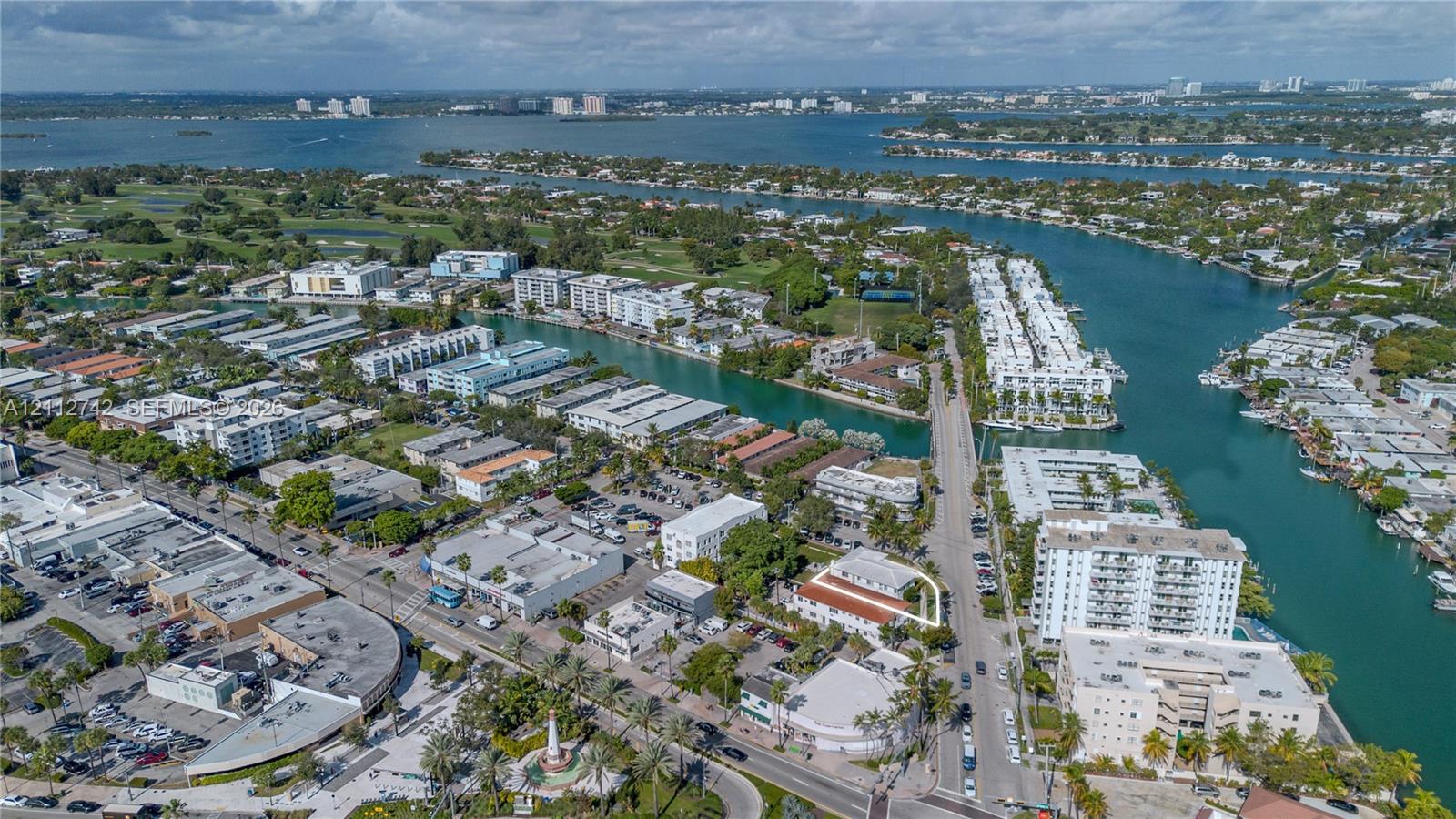 Aerial perspective of a multi-story property featuring a terra-cotta tile roof, perimeter landscaping, and a corner lot configuration within a coastal waterway district