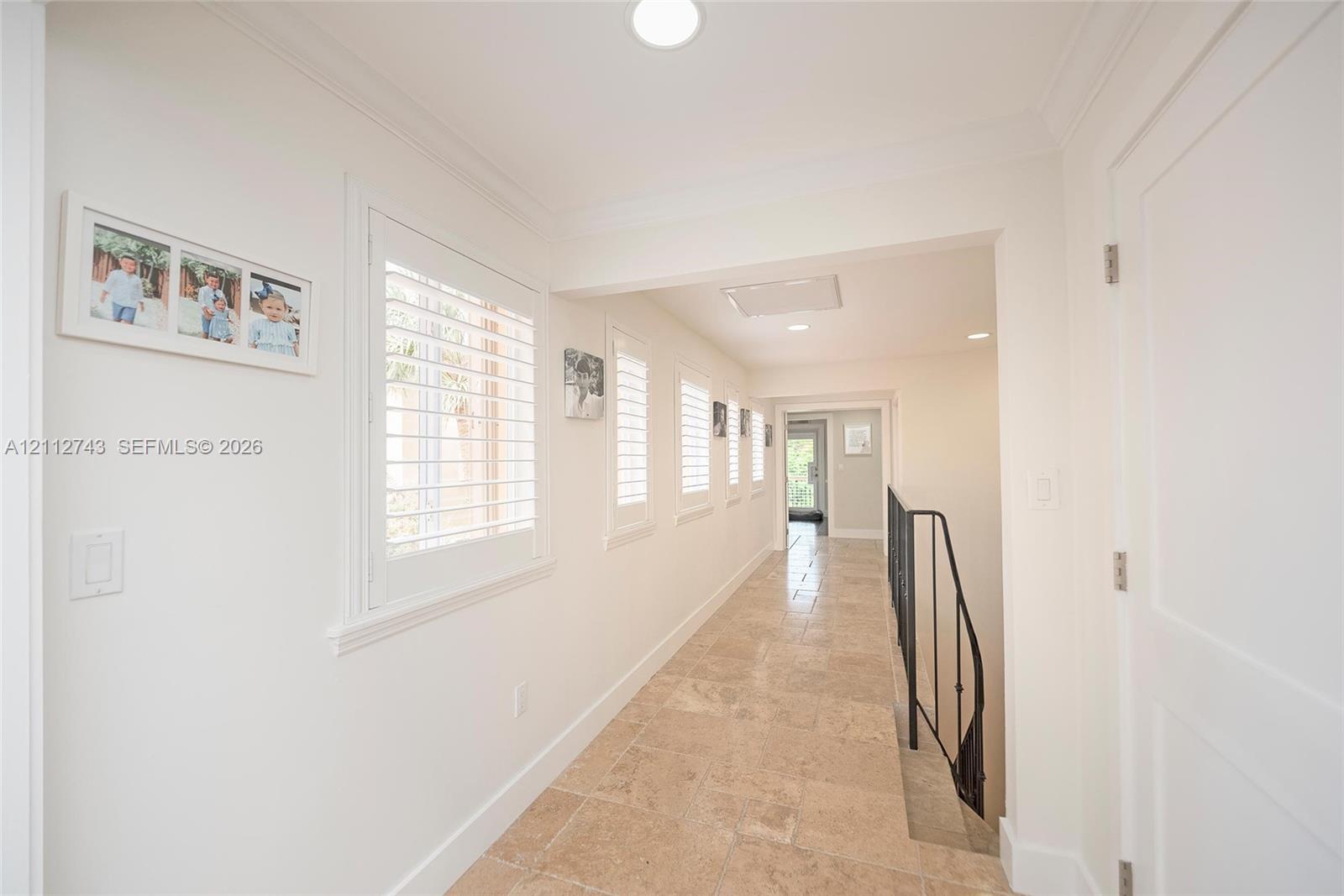 Hallway featuring stone tile flooring, plantation shutters, recessed lighting, and crown molding
