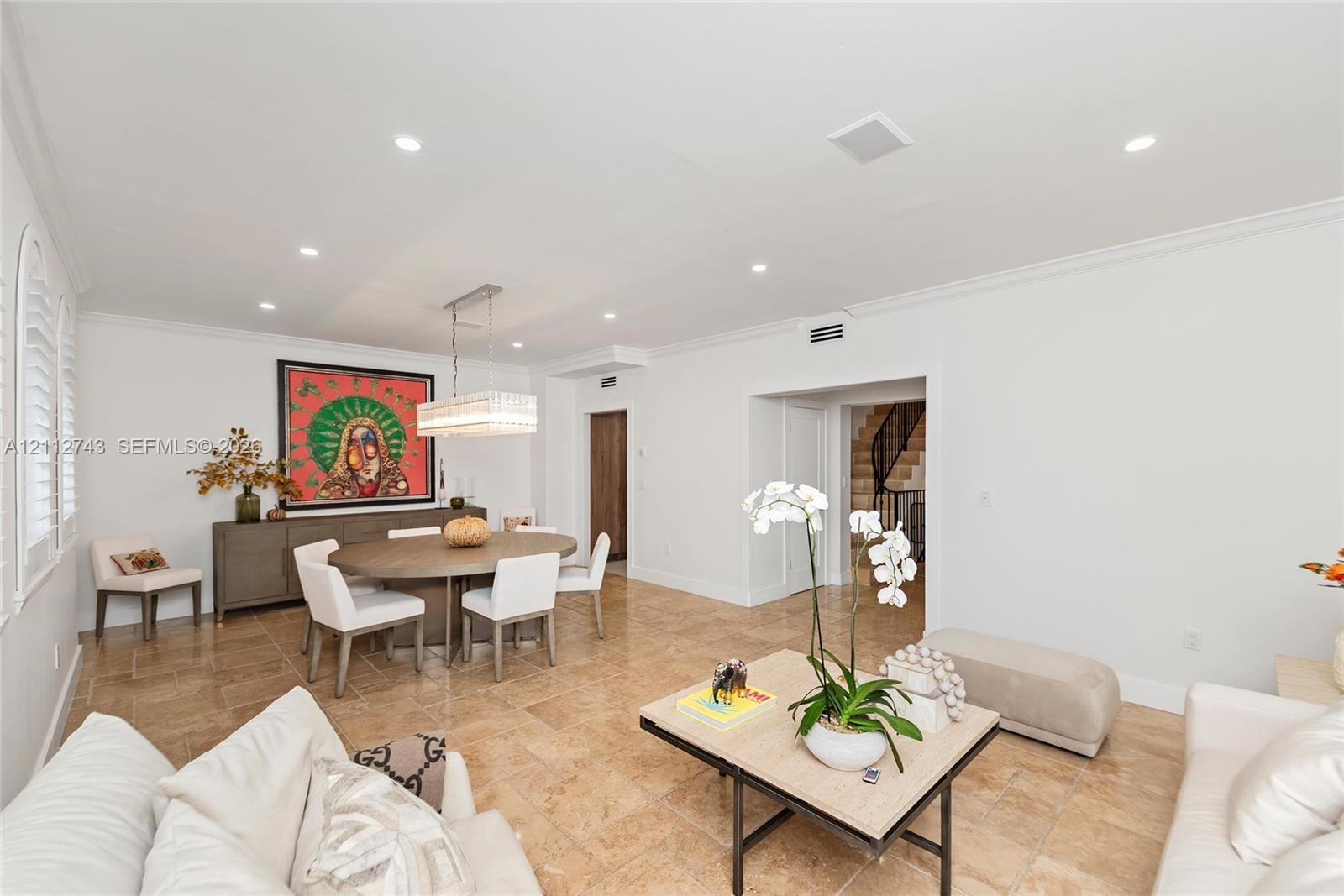 Open-concept area featuring stone tile flooring, crown molding, recessed lighting, and a rectangular multi-tiered crystal chandelier