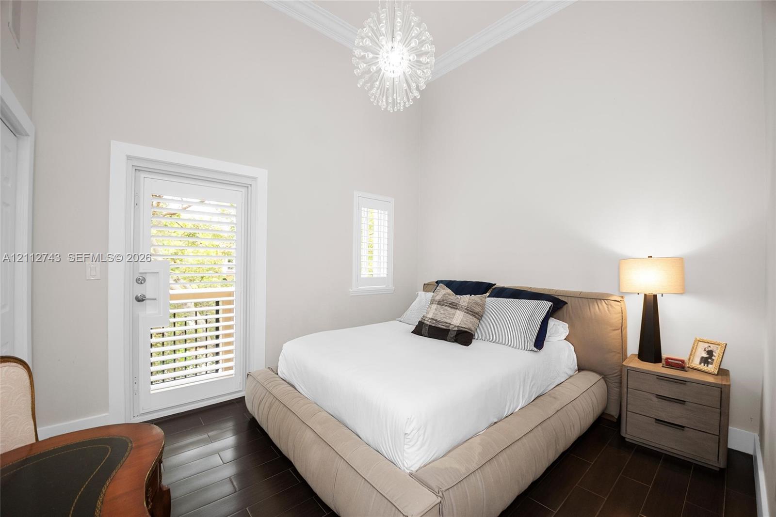 High-ceiling room featuring dark wood-finish flooring, crown molding, a multi-faceted crystal-style pendant light, and a door with integrated shuttered glass