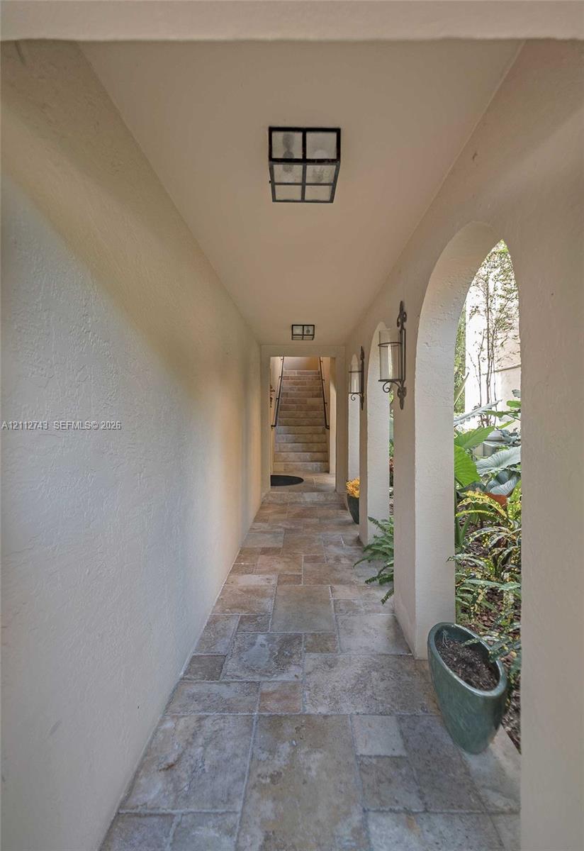 Covered walkway featuring a series of architectural arches, stone tile flooring, wall-mounted lantern-style lighting, and flush-mount overhead lighting