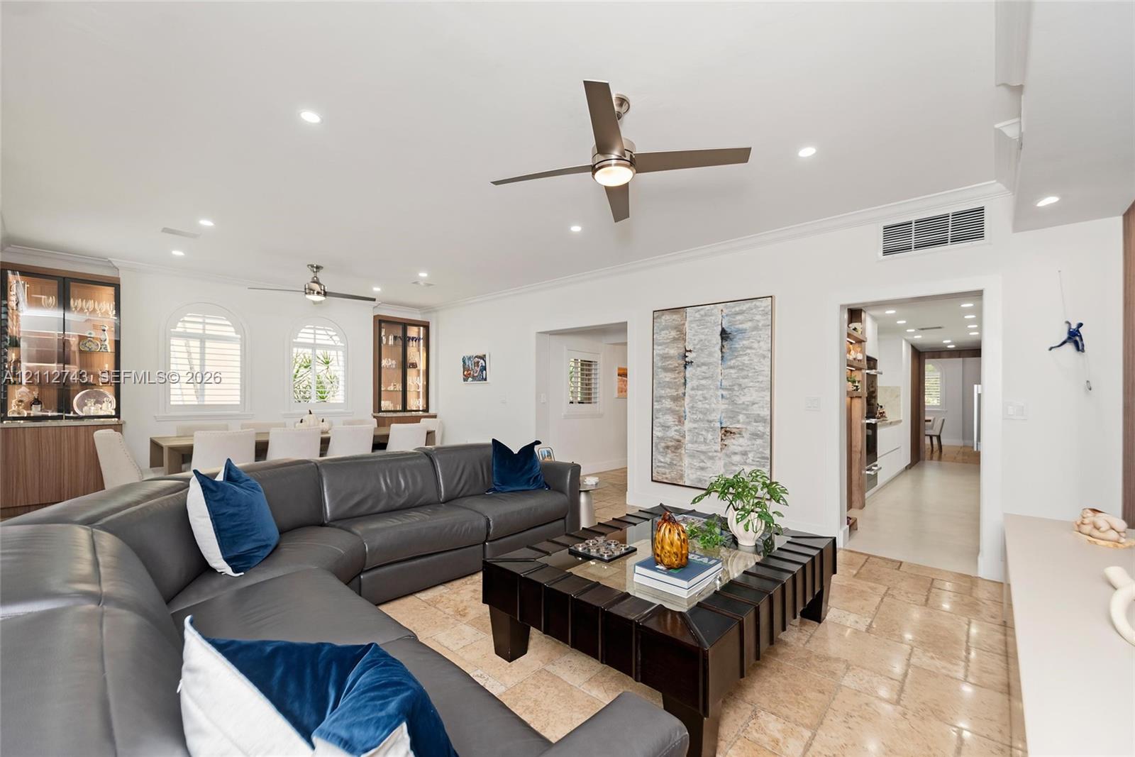 Open-concept interior featuring natural stone flooring, recessed lighting, ceiling fans, arched windows, and built-in cabinetry with glass-front display shelves