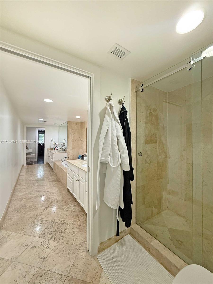 Bathroom featuring large-format tile flooring, a glass-enclosed shower with stone tile surround, and built-in cabinetry with a stone countertop