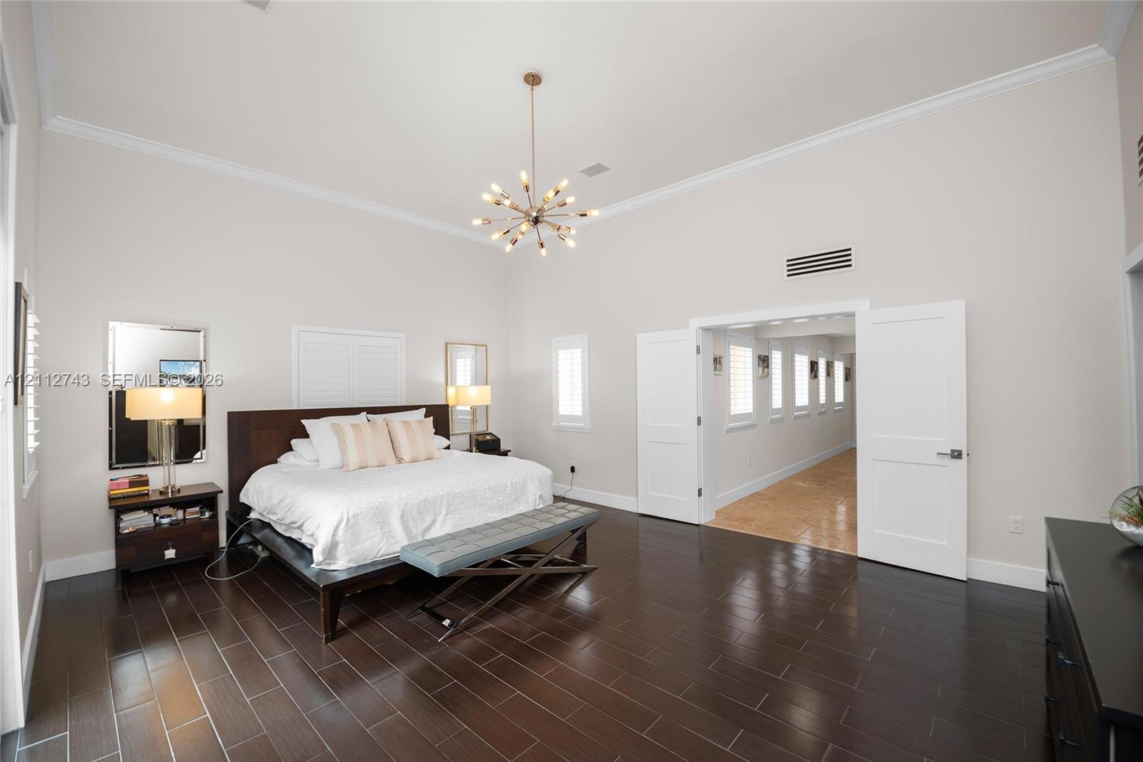 High-ceilinged room featuring dark wood-finish tile flooring, crown molding, multi-light metallic chandelier, and double doors opening to a secondary space