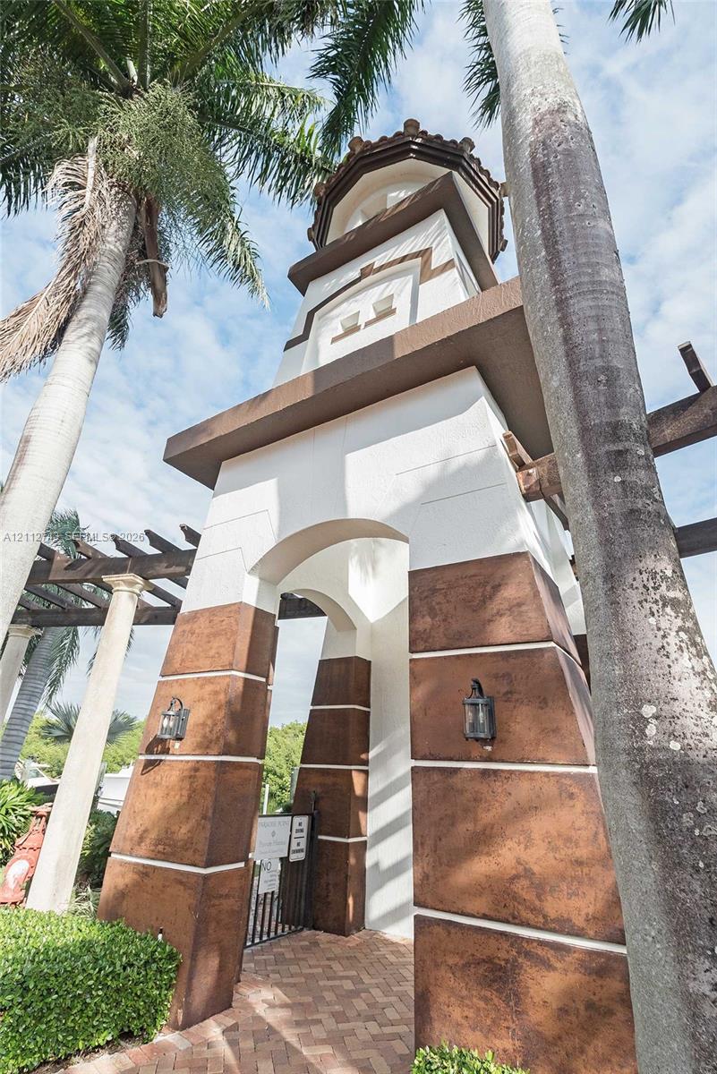 Architectural tower featuring a stucco exterior, decorative stone-finish base, arched entryway, and attached lantern-style lighting fixtures, set atop a paver walkway