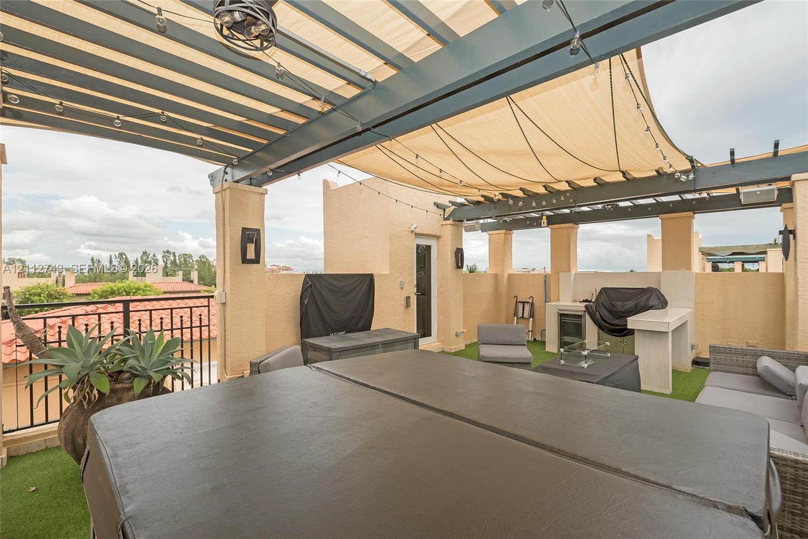 Rooftop terrace featuring a covered pergola with a retractable shade canopy, built-in outdoor kitchen, integrated lighting, and artificial turf flooring