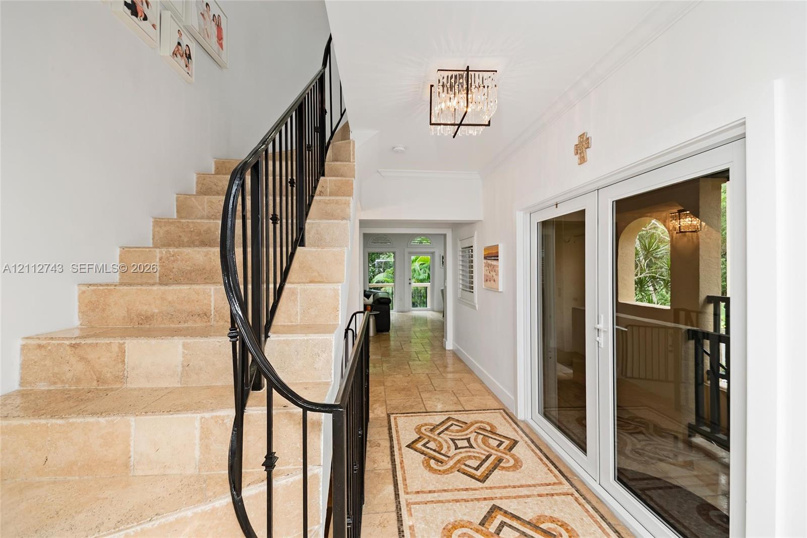 Foyer featuring stone tile flooring with decorative geometric inlay, a custom wrought-iron staircase railing, and a tiered crystal chandelier