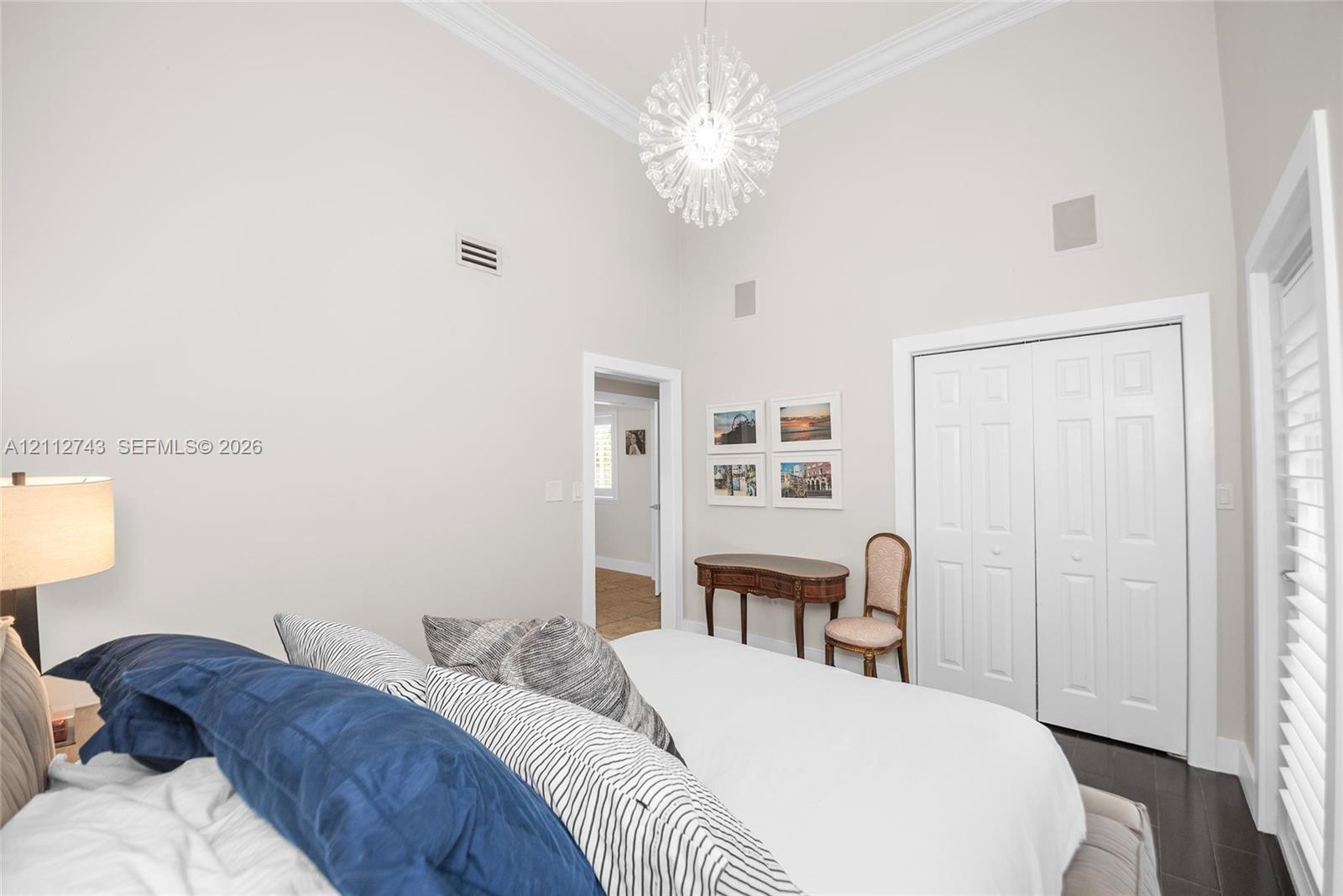 High ceilings featuring crown molding, a decorative crystal-style chandelier, double-panel closet doors, and plantation shutters