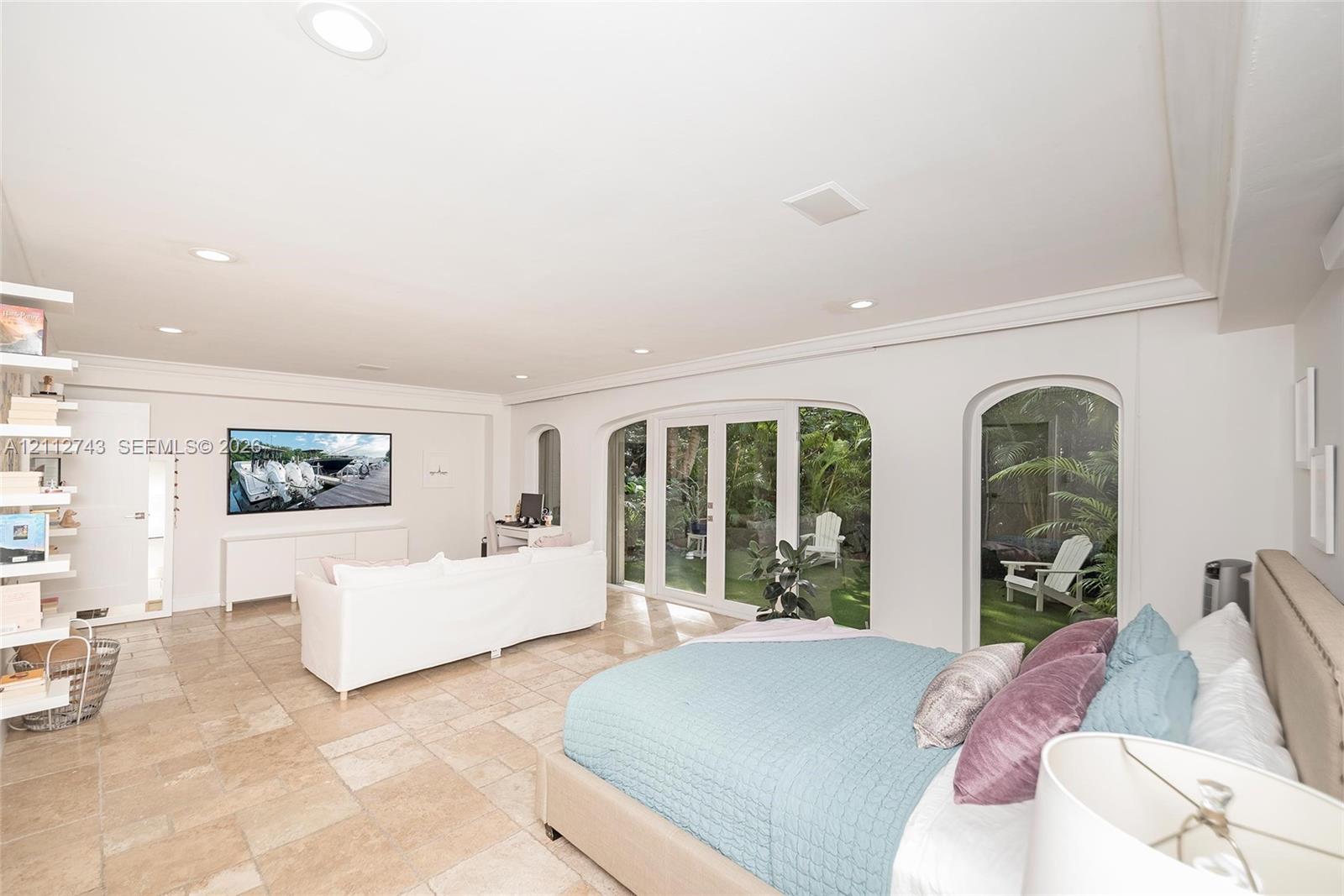 Spacious room featuring light-toned tile flooring, recessed lighting, built-in shelving, white French doors, and arched glass inserts