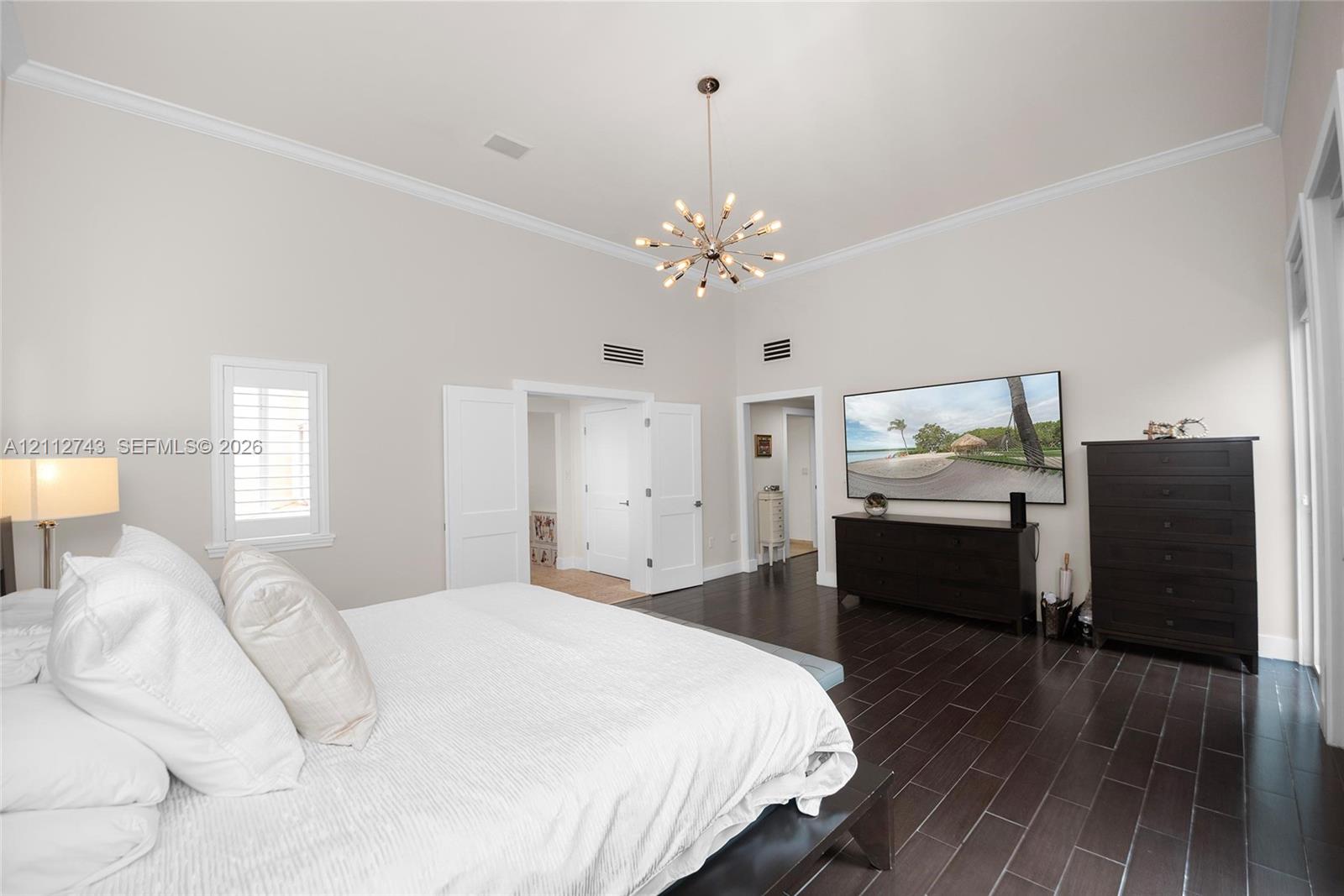 High ceilings featuring crown molding, dark wood-finish flooring, and a modern sputnik-style chandelier