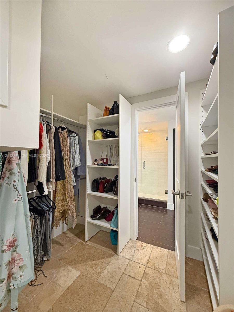Walk-in closet featuring custom white built-in shelving, hanging rods, and natural stone tile flooring