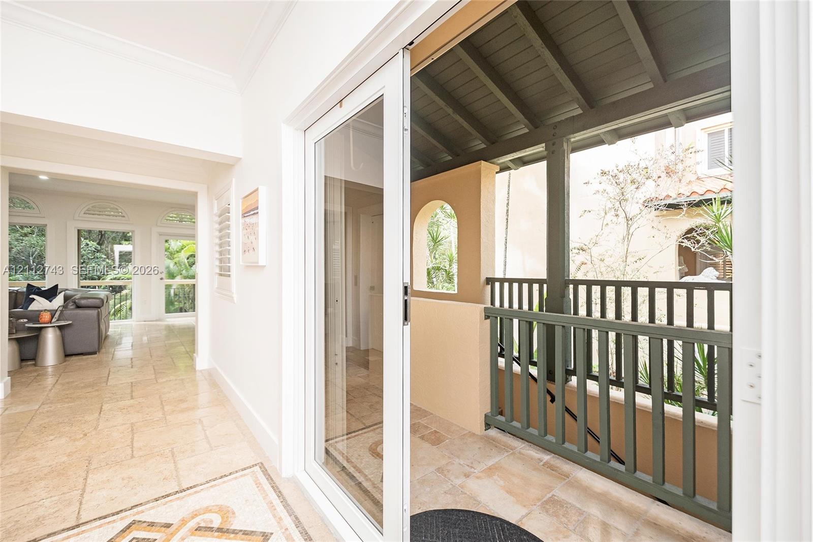 Covered balcony featuring stone tile flooring and a vertical balustrade, accessed through full-height sliding glass doors