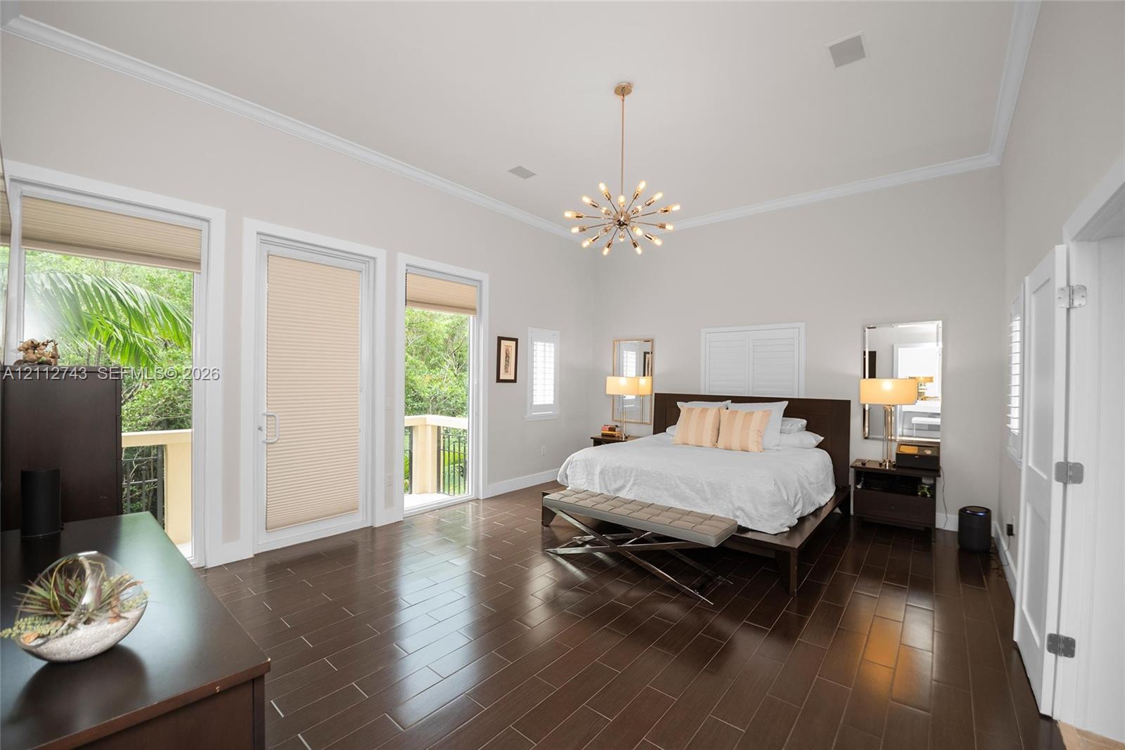High ceilings with crown molding, wood-finish flooring, two glass-paneled exterior doors, and a decorative multi-bulb chandelier