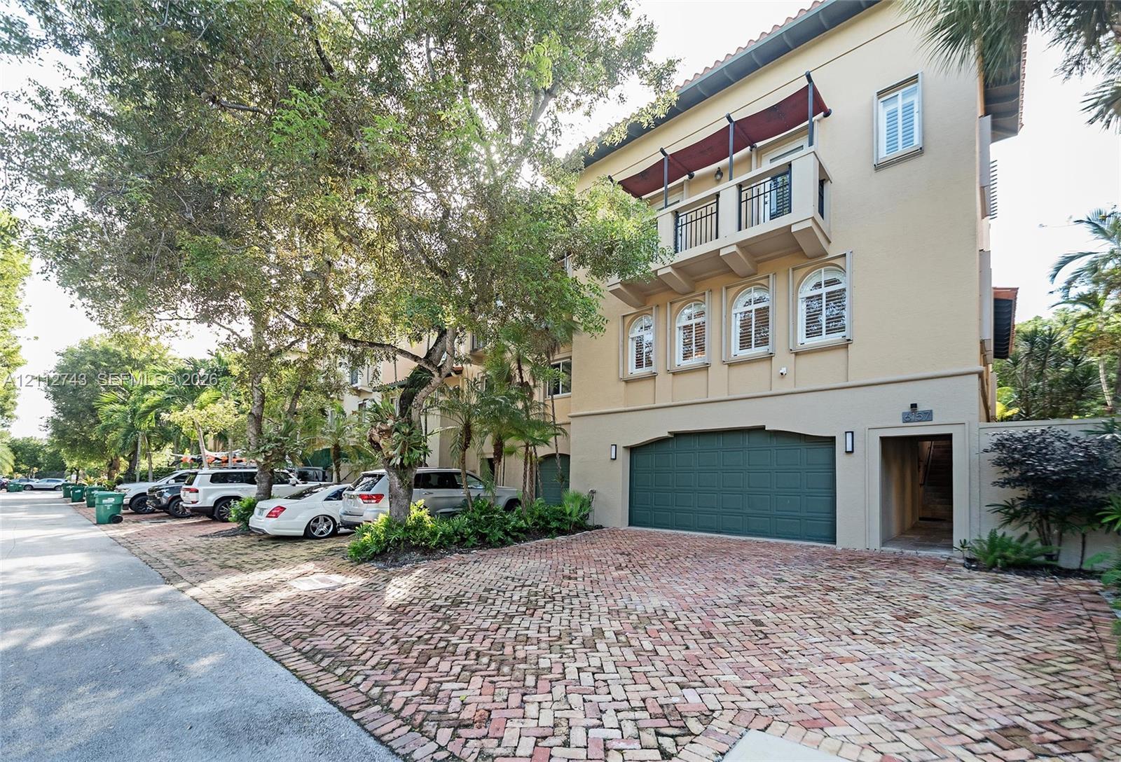 Three-story exterior featuring a brick-paved driveway, multi-car garage with arched detailing, balcony with metal railing, and arched window accents