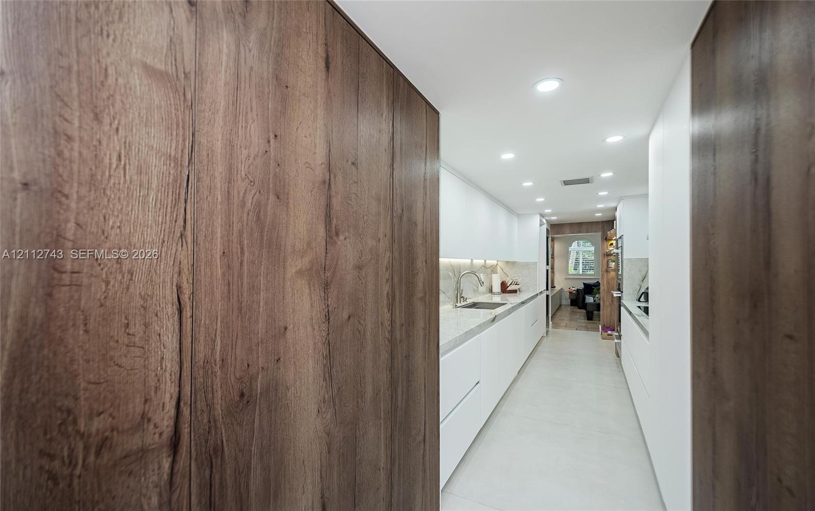 Modern kitchen featuring flat-panel white cabinetry, stone-finish countertops, wood-finish paneling, recessed lighting, and under-cabinet illumination
