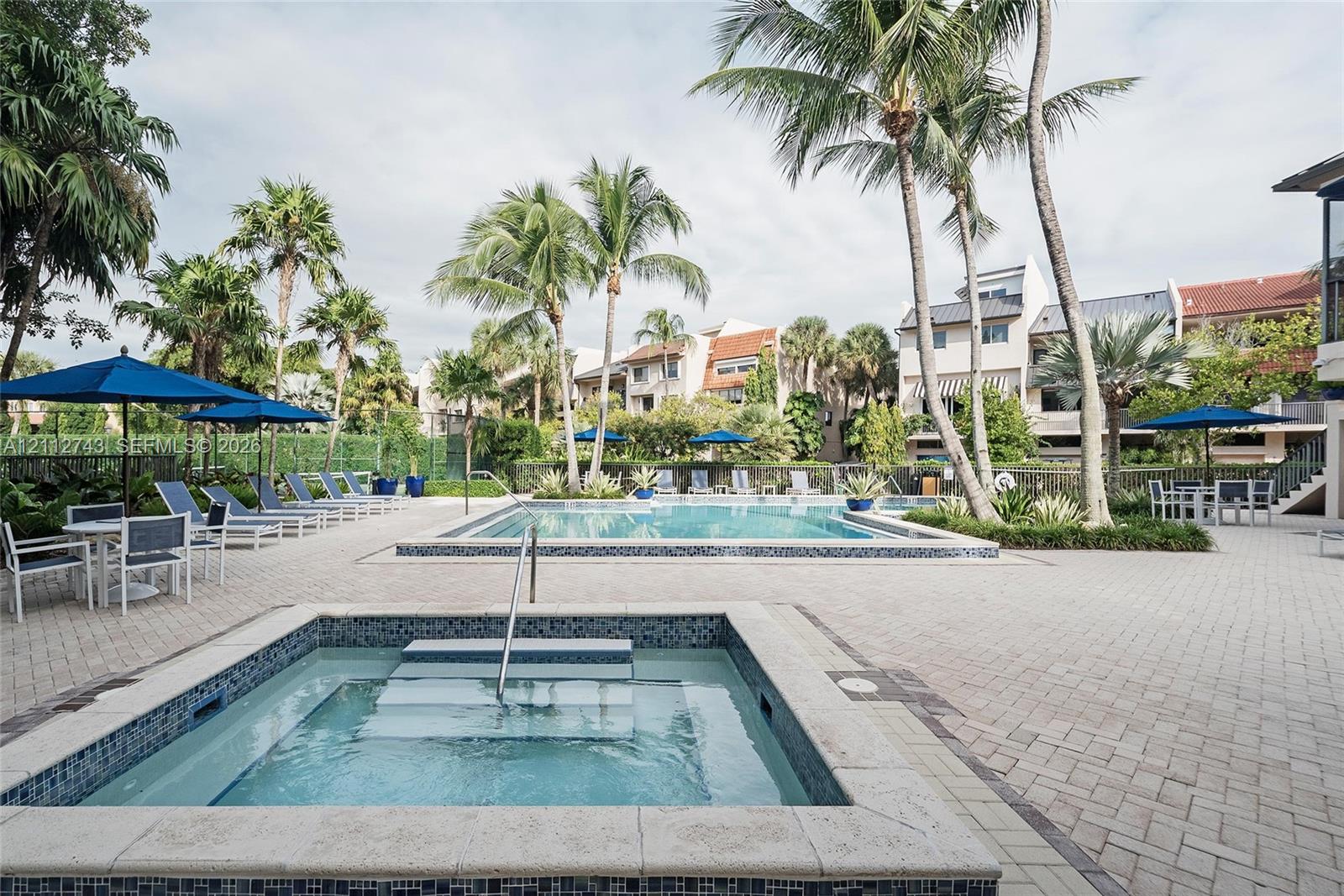 Outdoor swimming pool and spa featuring a stone-paver deck, built-in steps, and surrounding palm trees
